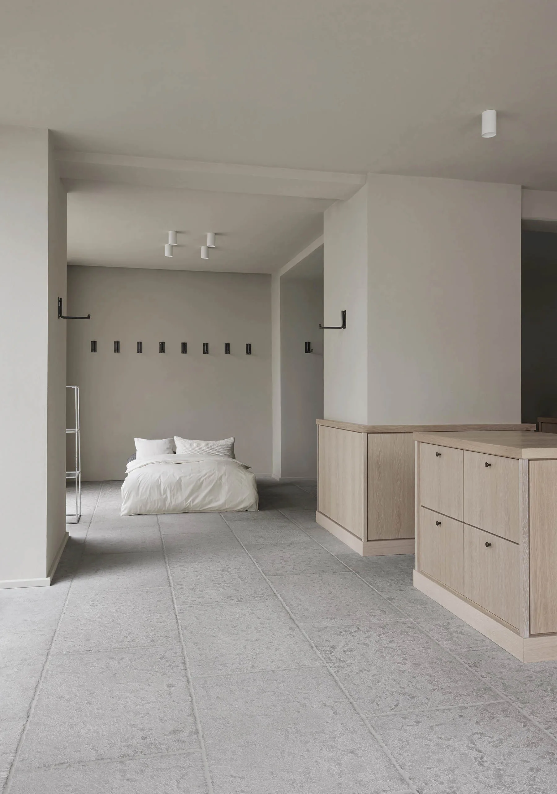 A minimalist bedroom features a white bed with a concrete floor