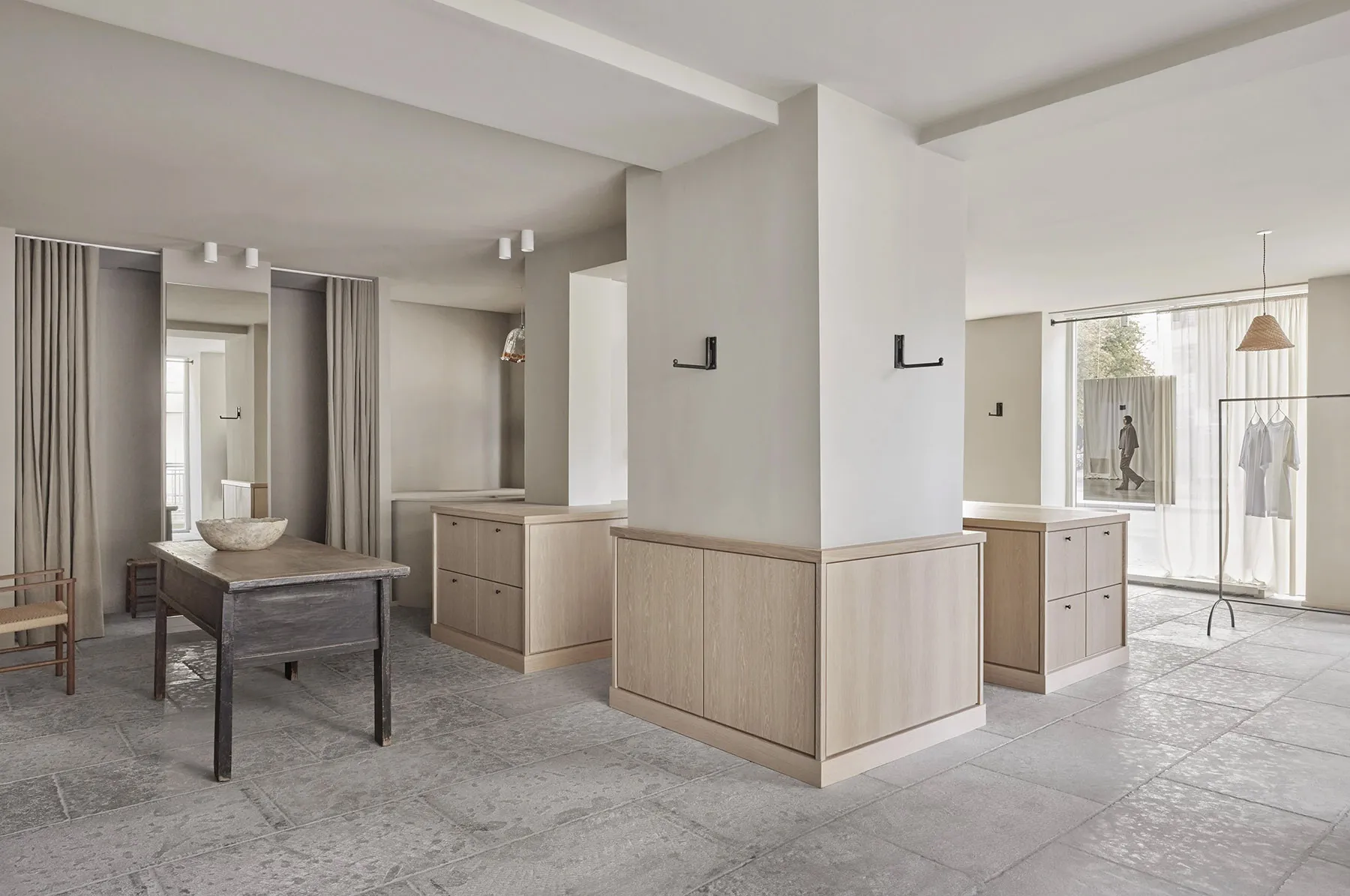 Modern minimalist retail store interior with concrete floor, wooden furniture, and glass display cases.