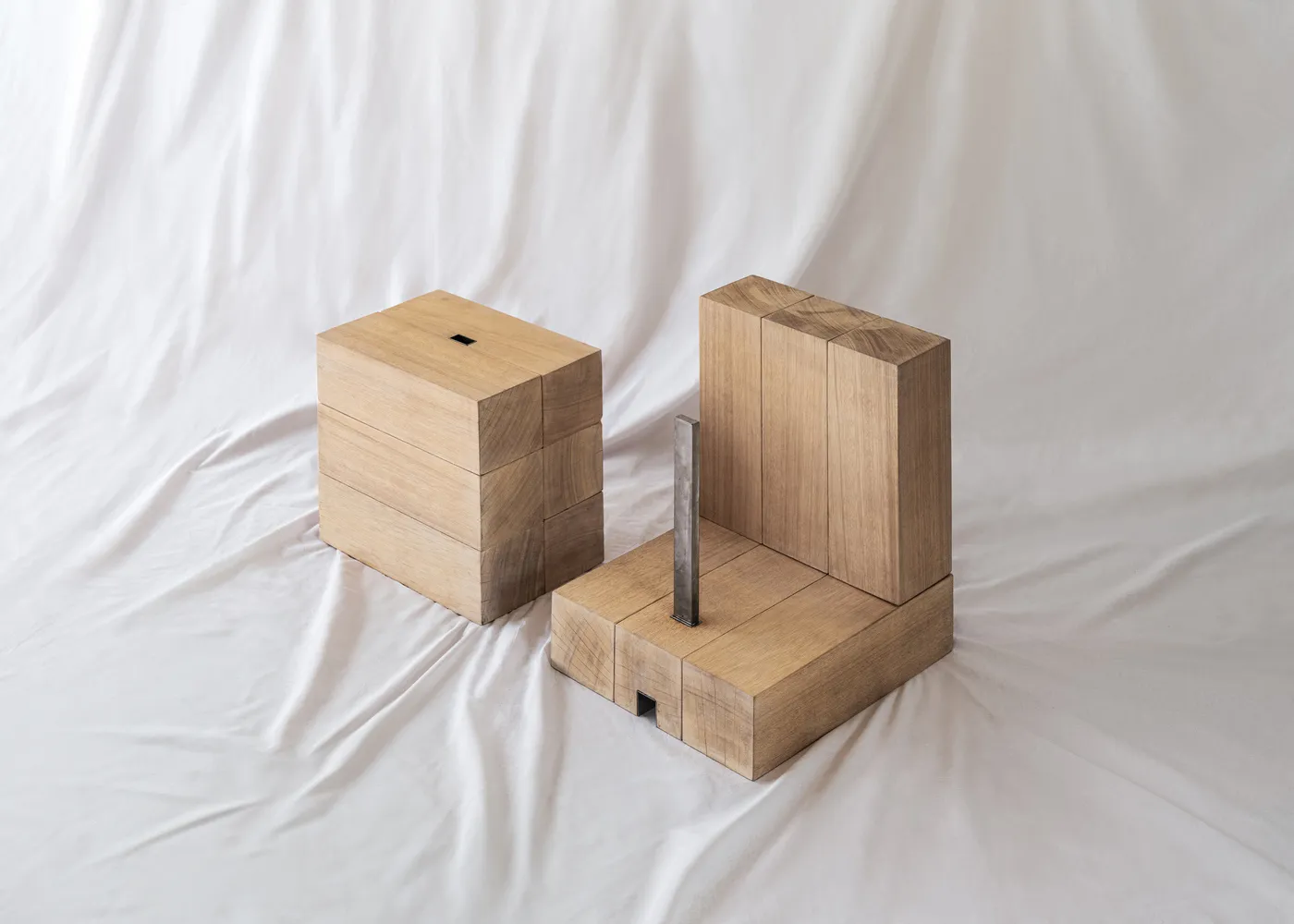 Two minimalist wooden blocks with a metal rod, placed on a white fabric background.