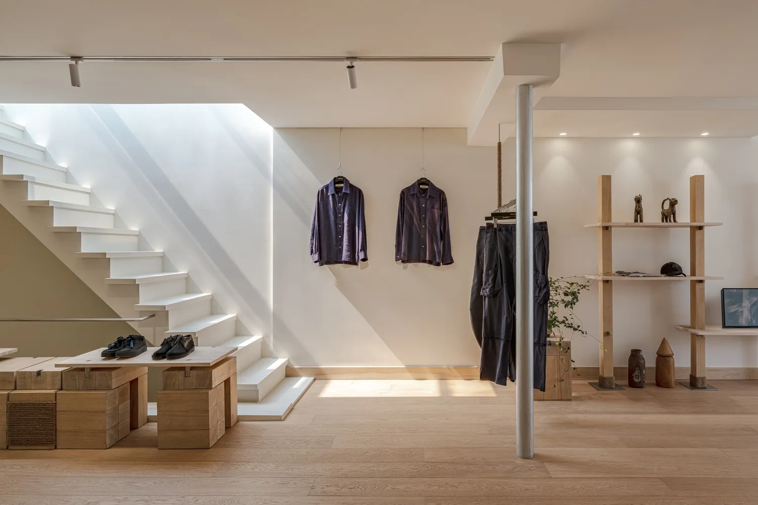 A minimalist retail store with neutral materials, featuring a display area with clothing hanging on the wall and shoes on the