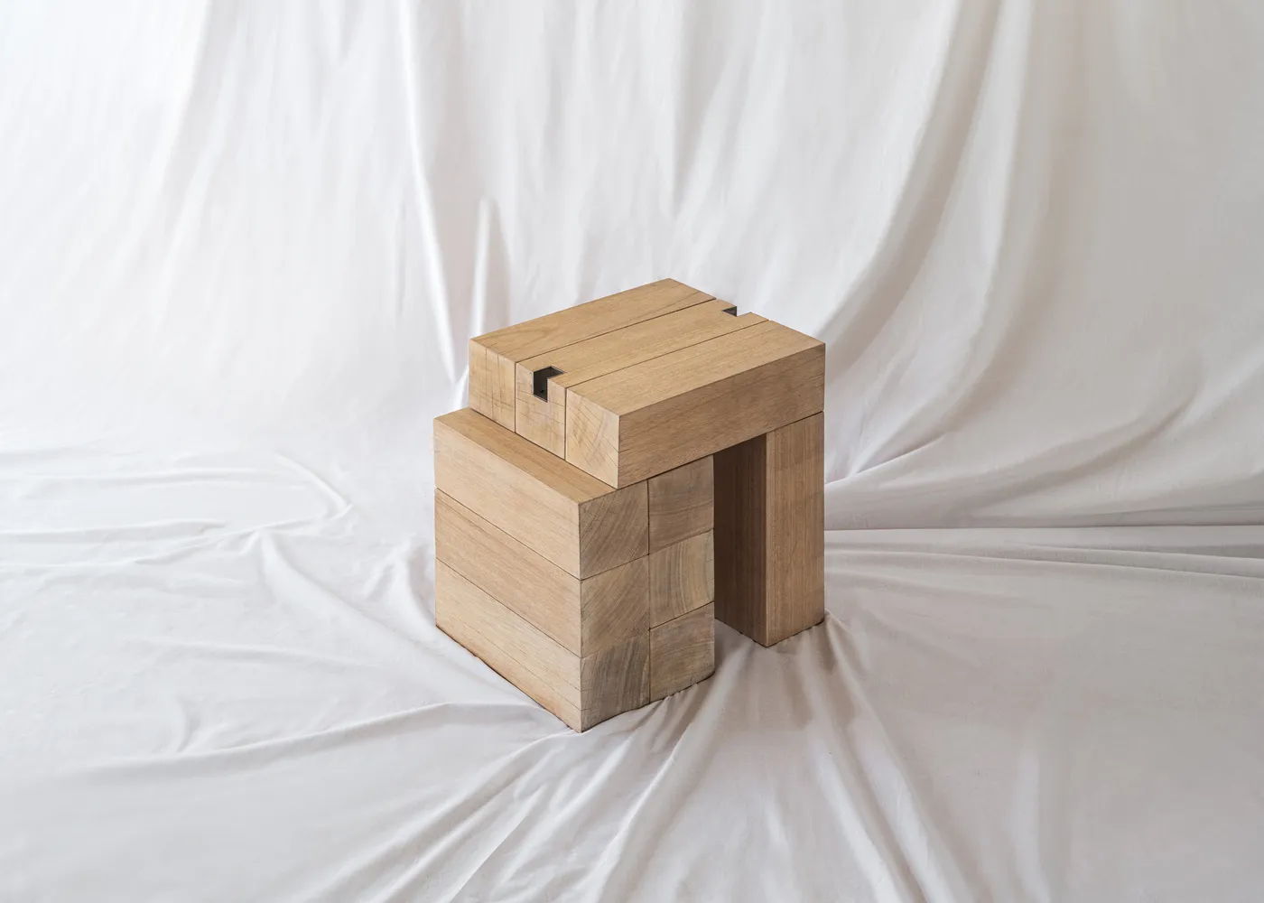 A minimalist design featuring stacked wooden blocks with metal connectors, placed on a white fabric background.