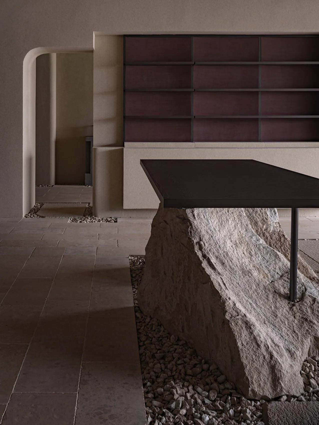 A modern bench featuring a unique design with a rock base, placed in a minimalist space with a concrete wall and floor.