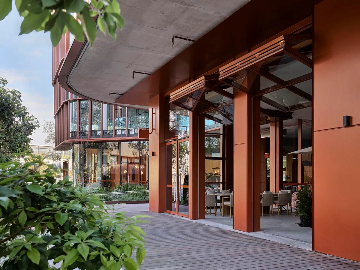 Modern restaurant entryway featuring wooden flooring, concrete structural columns, and large glass windows.