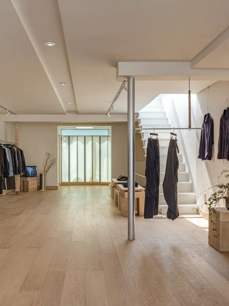 An interior view of a modern retail store featuring a white wooden floor, white concrete stairs, and minimalist design.