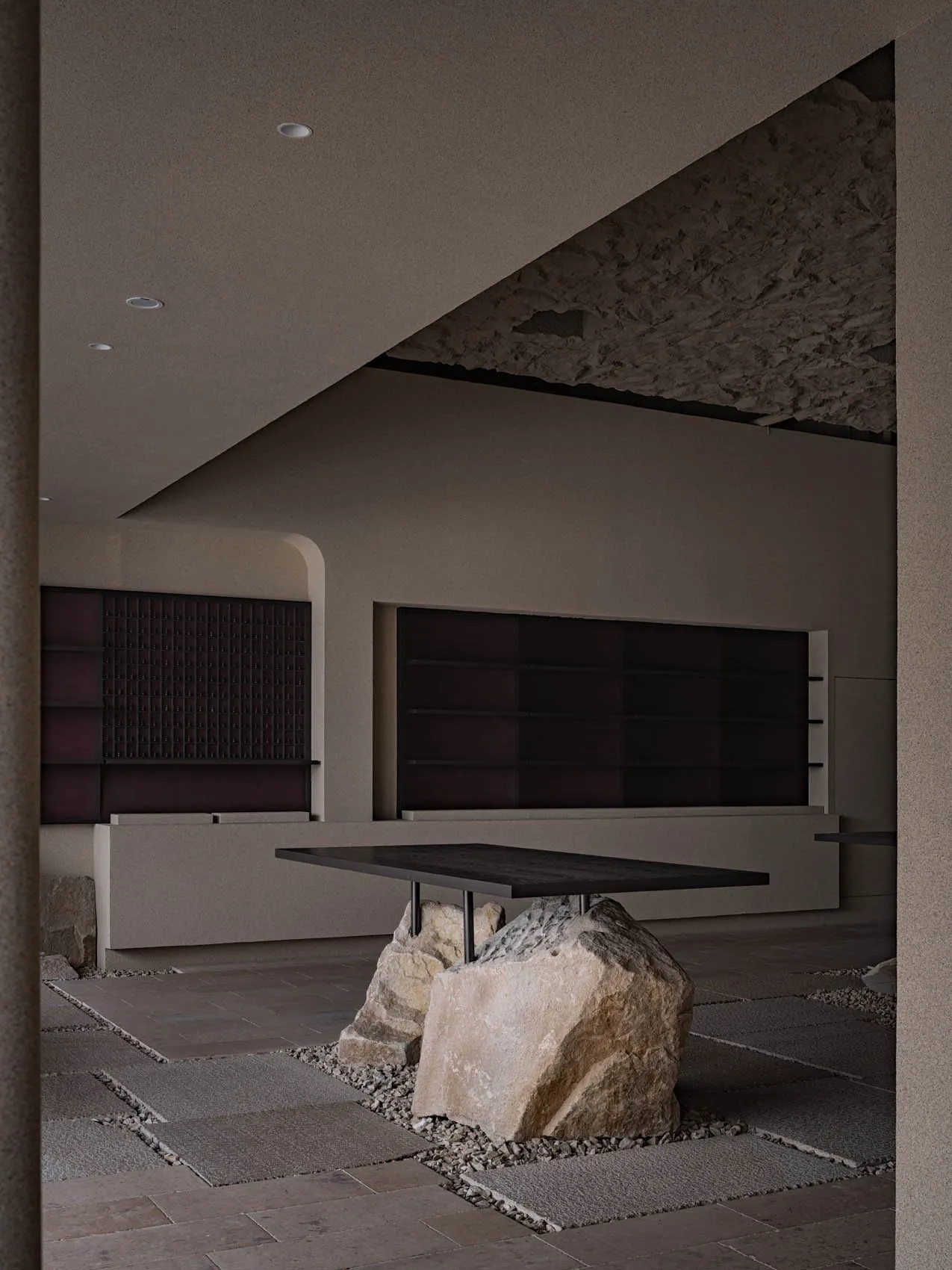 A minimalist interior space featuring a concrete table surrounded by large rocks, with dark walls and a low ceiling.