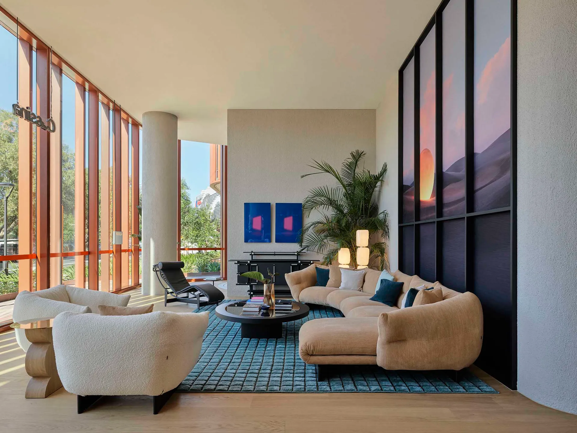 A modern minimalist living room with a plush fabric couch, two plush white armchairs, and a wooden coffee table on a blue rug