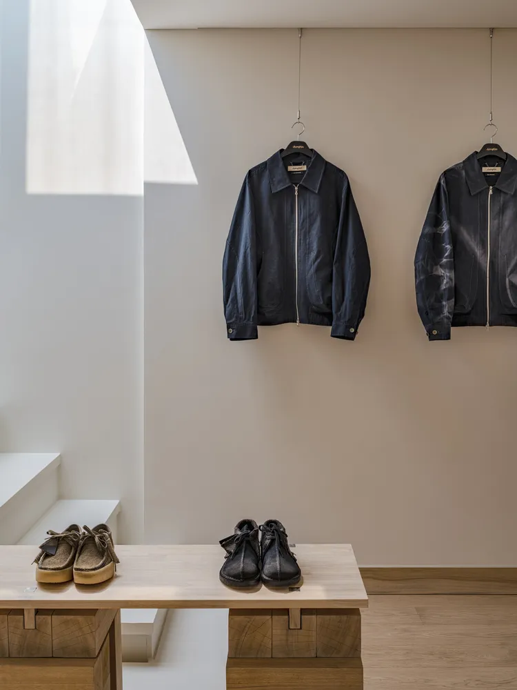 Clothing shop interior with wooden elements, featuring jackets on display and shoes on a table.