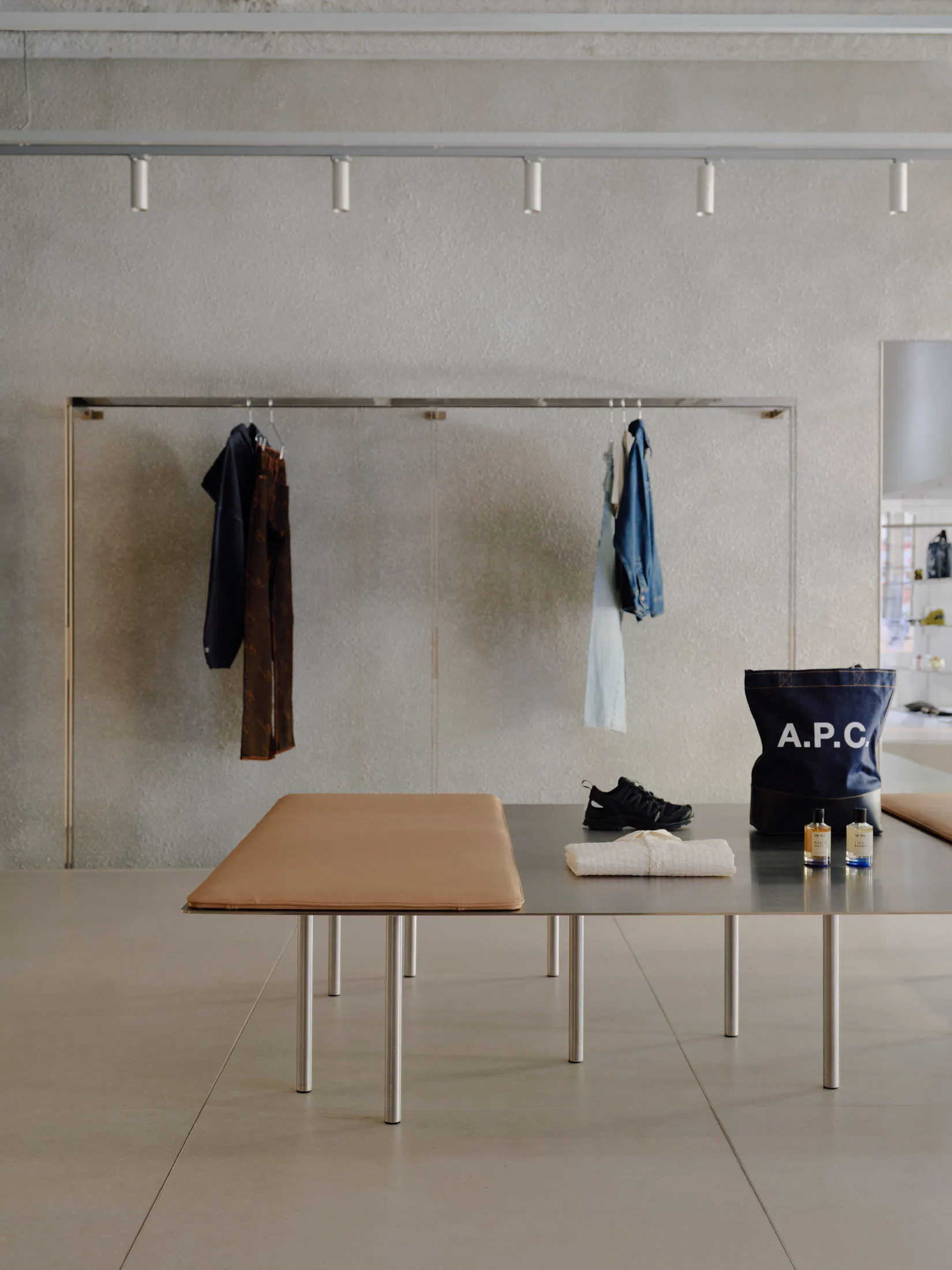 A minimalist setting featuring a metal bench and table showcasing clothing items and accessories.