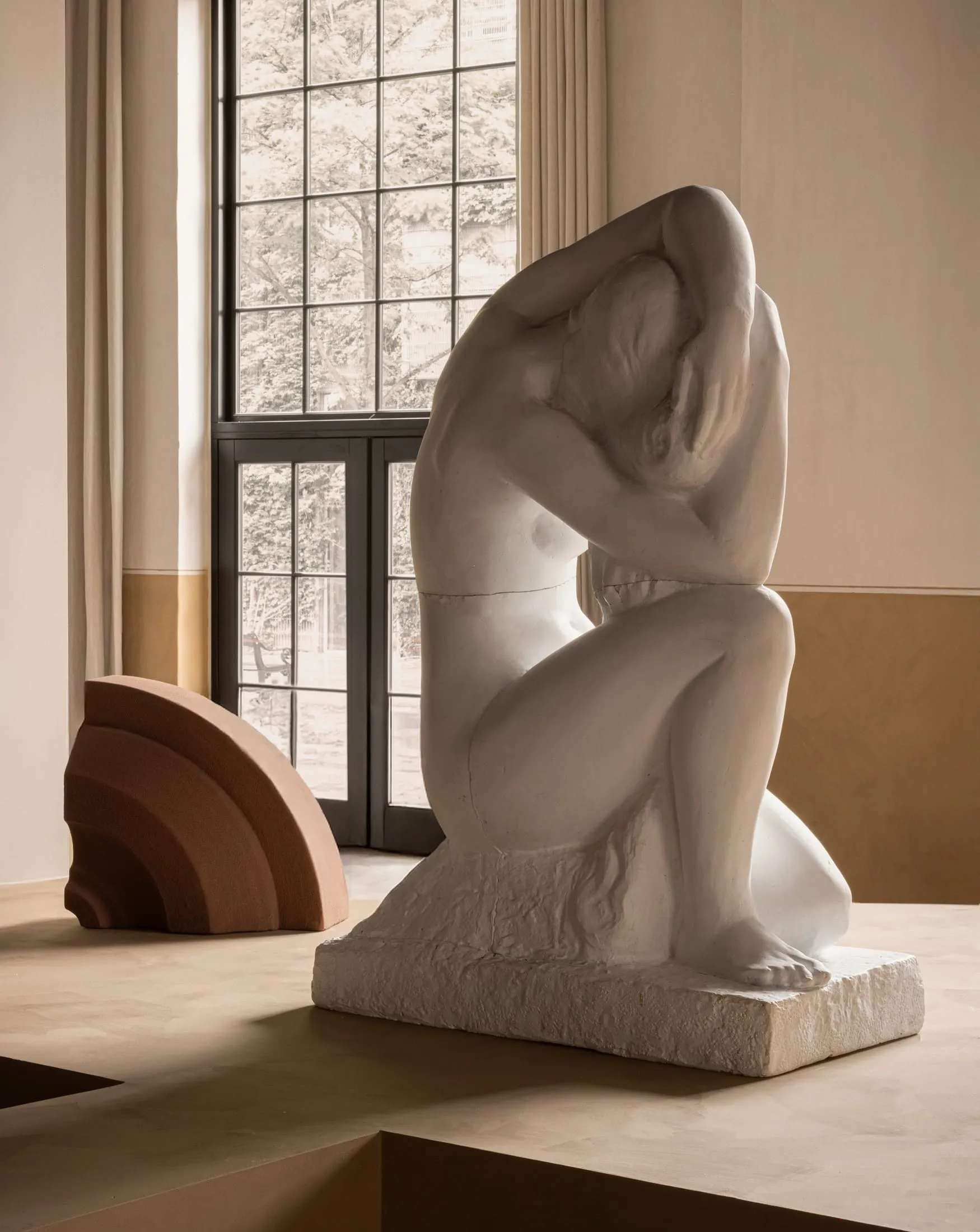 A large abstract sculpture made of stone, featuring a gestural pose with exaggerated forms and smooth, flowing lines.