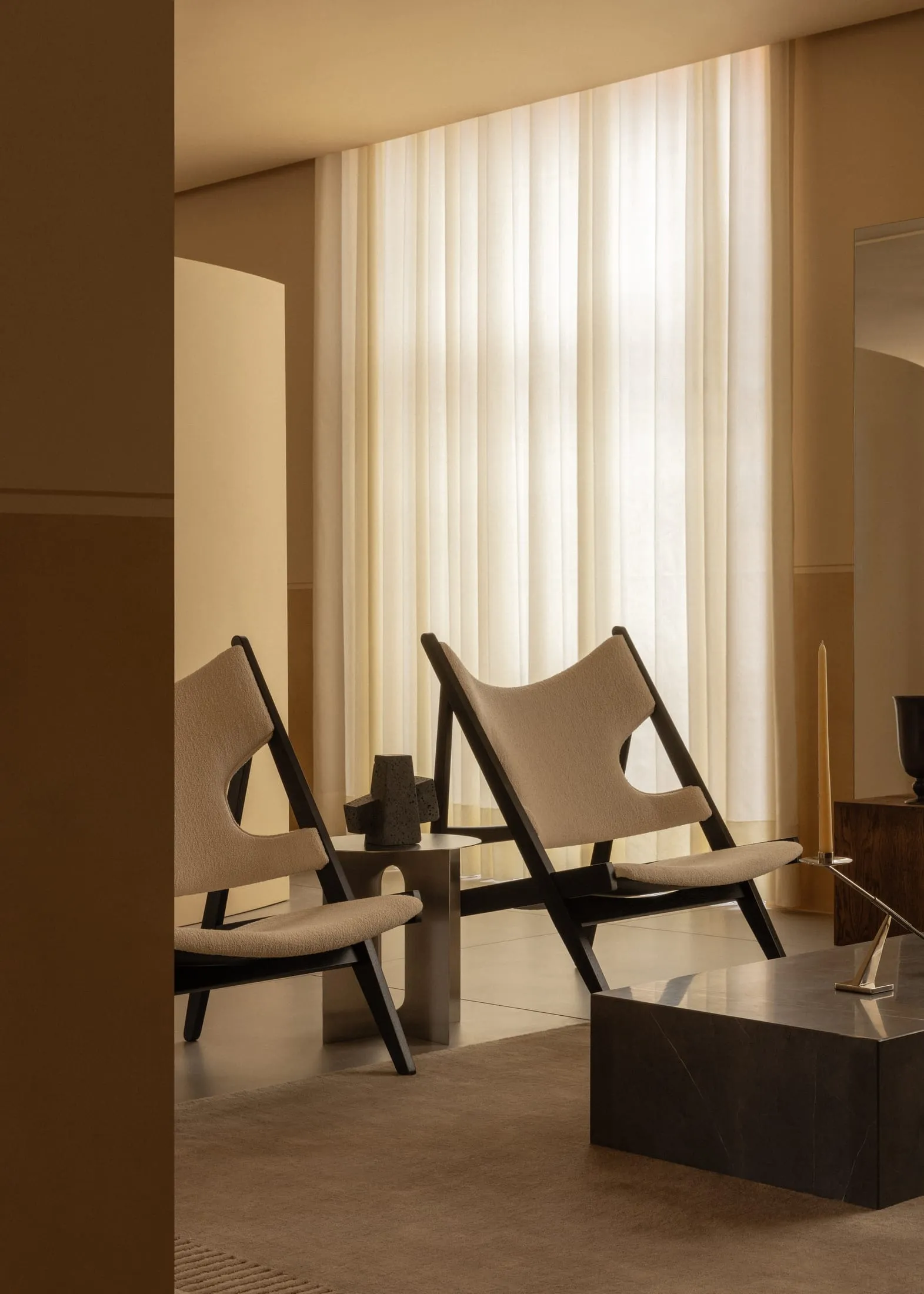 Two modern minimalist armchairs upholstered in fabric placed in front of a large window with sheer curtains, featuring a meta