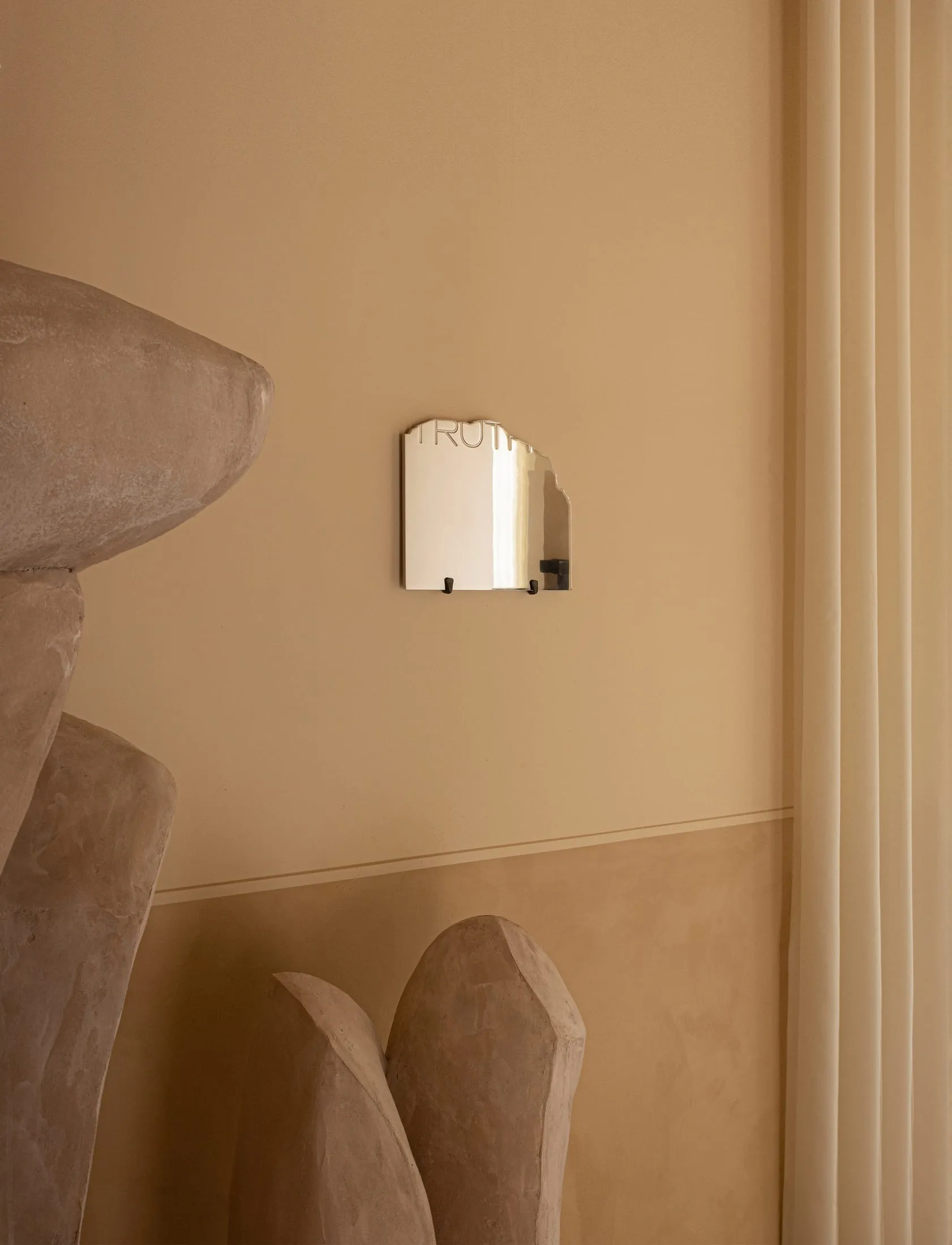 A minimalist, geometric mirror with the word 'truth' on a metallic surface, mounted on a beige wall.