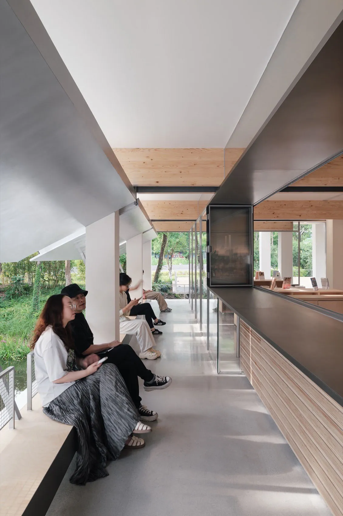 People sitting on benches in a modern glass-walled interior space.