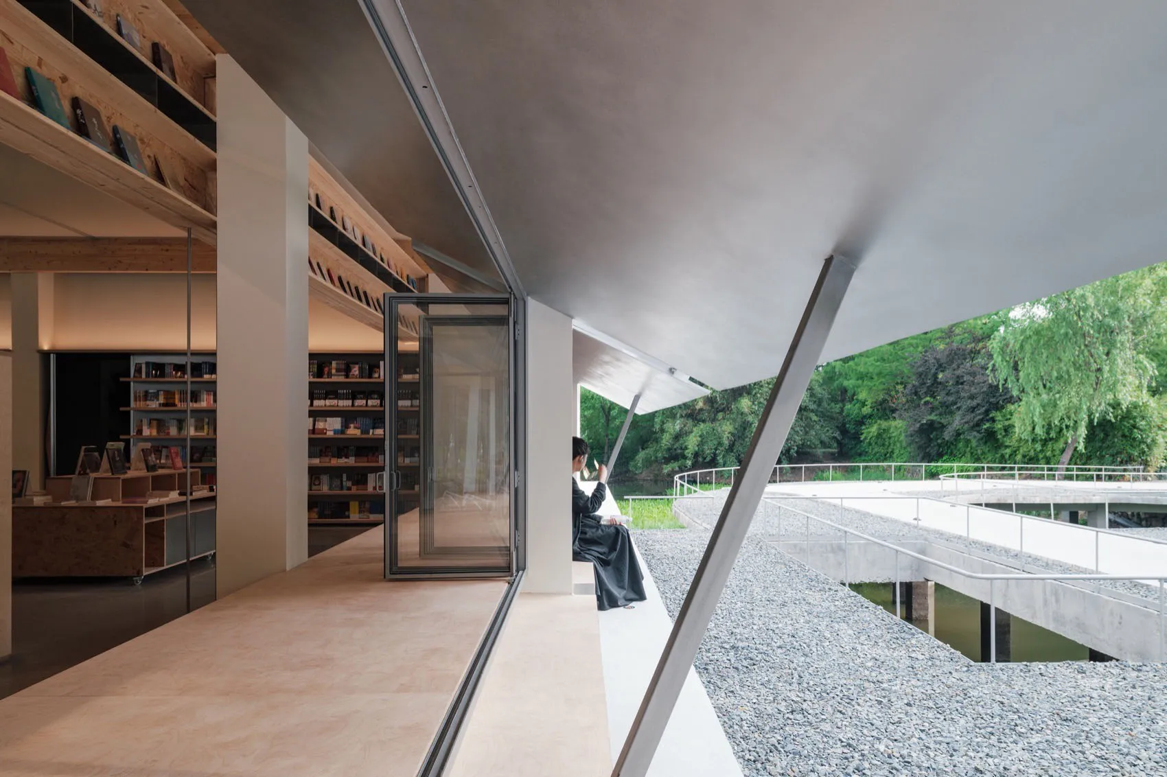 A modern library with concrete walls and a glass door overlooking a water body and greenery.