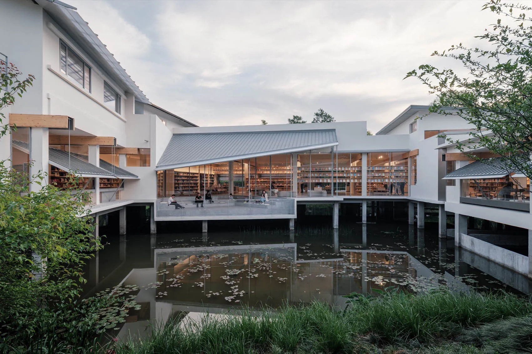 Modern library exterior featuring glass walls, wooden accents, and a concrete platform surrounded by water.