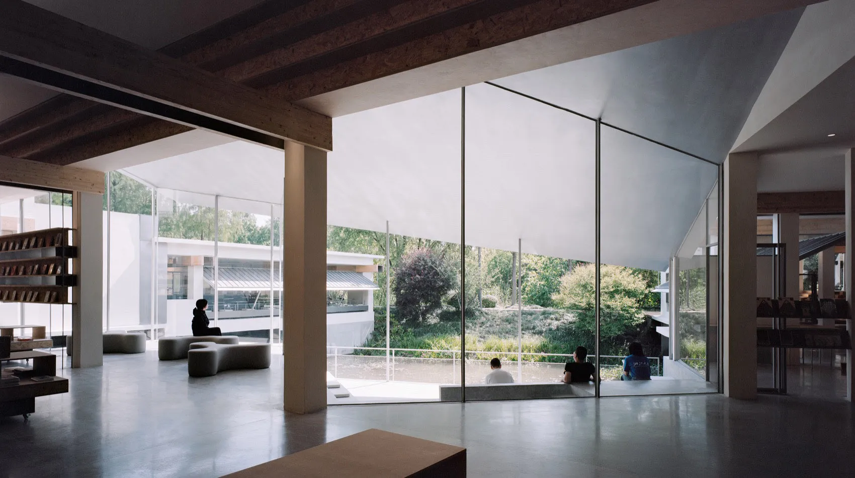 Modern library interior with glass walls, concrete floor, and wooden beams