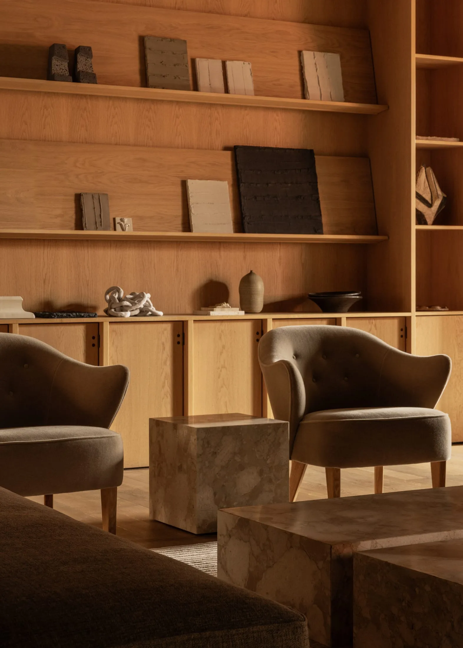 A modern living room featuring wood-paneled walls, marble coffee tables, and plush upholstered chairs.