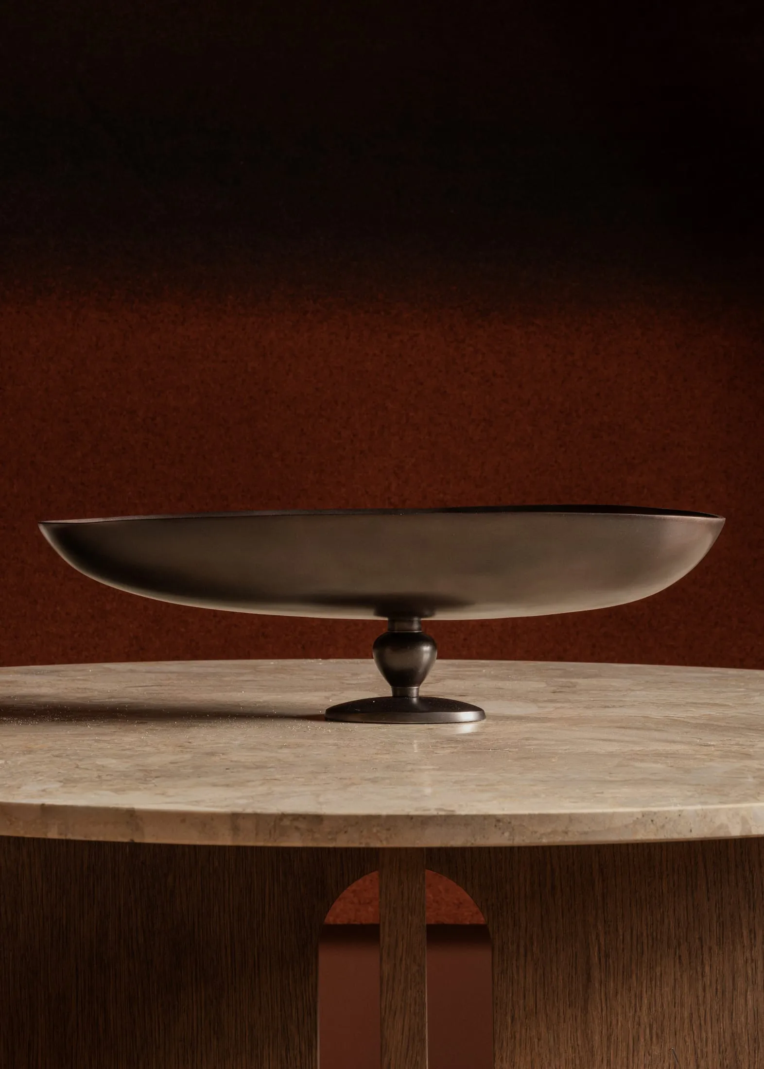 A sleek, modern metal decorative object on a marble table with a textured red wall background.