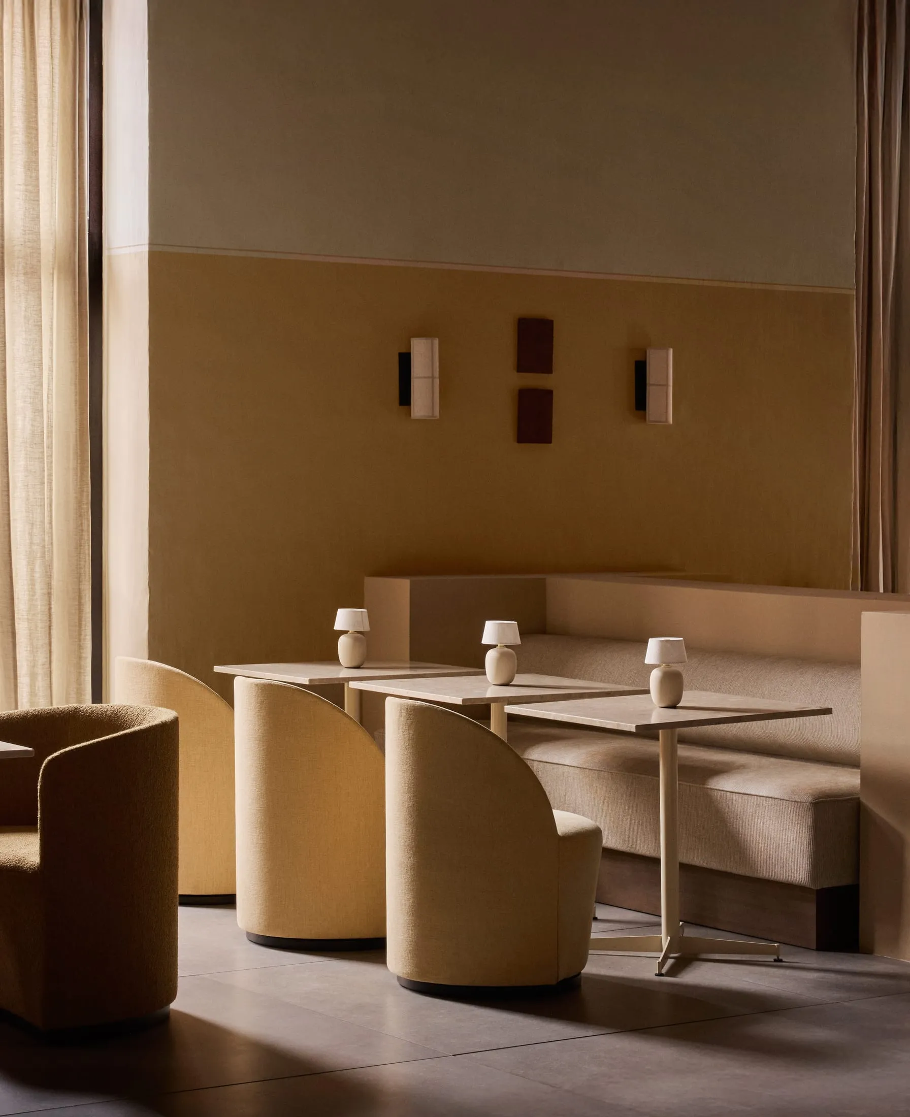A modern restaurant lounge with fabric seating, concrete tables, and white lampshades.
