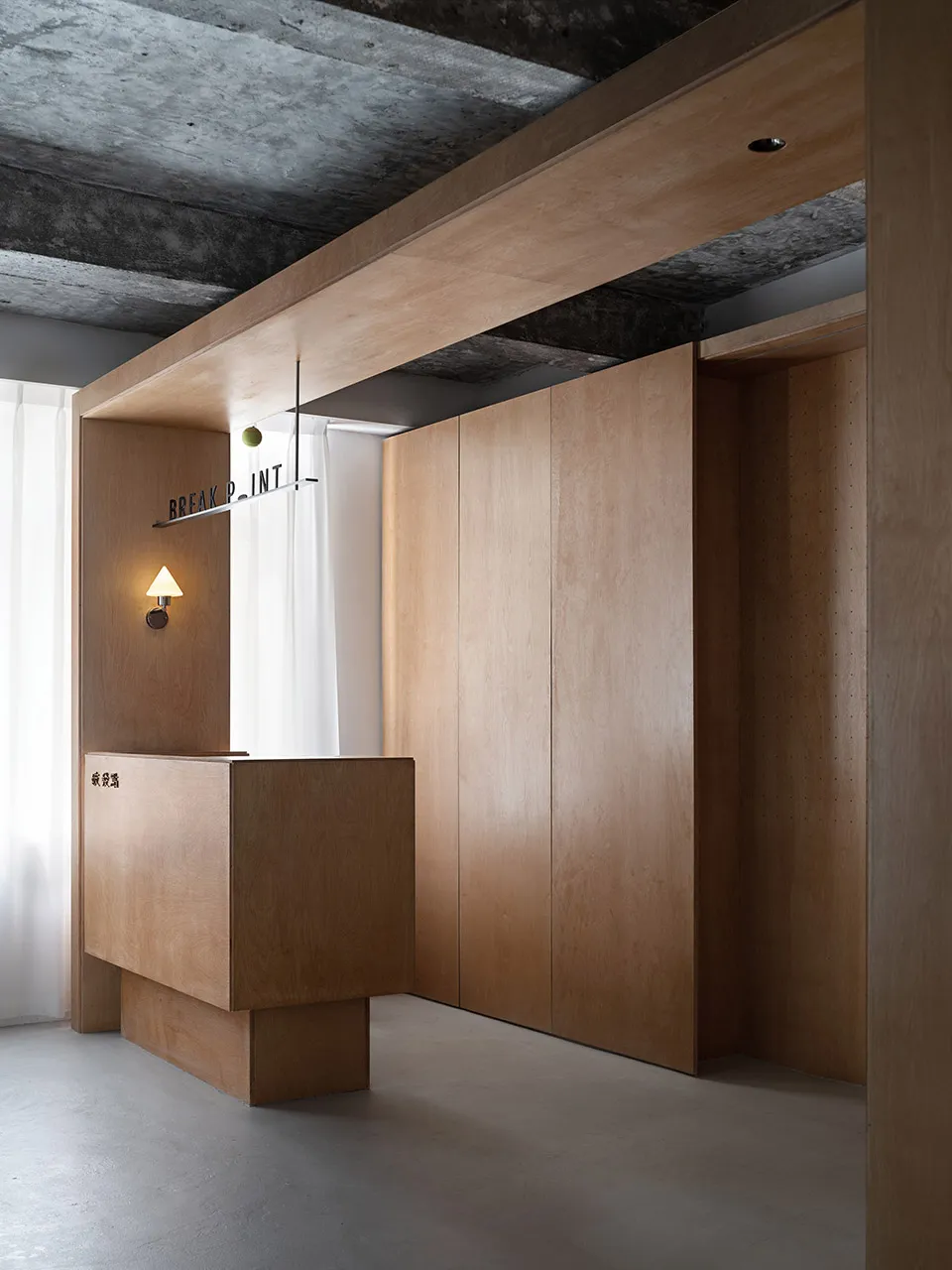 A minimalist office lobby with a wooden reception desk and concrete ceiling beams.