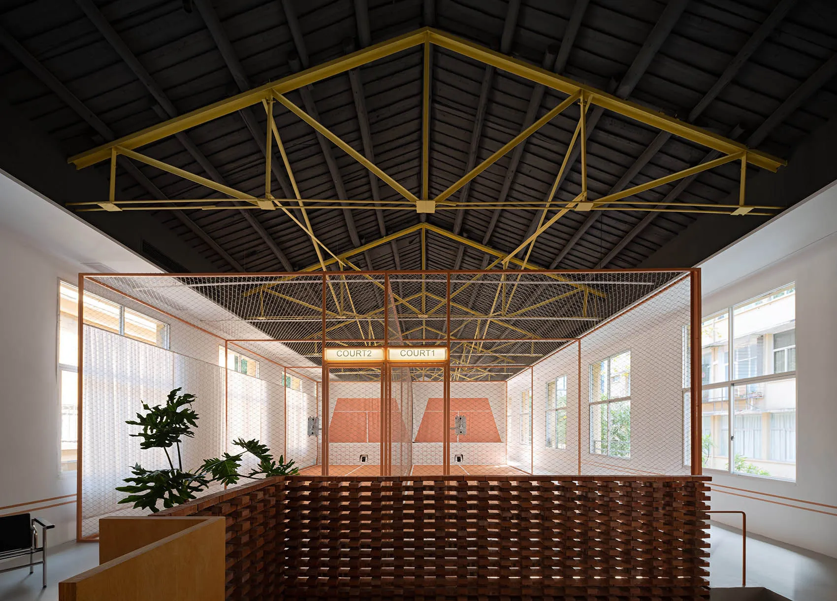 An indoor sports facility with a high ceiling, brick walls, and a grid of metal tubing dividing the space into two courts.