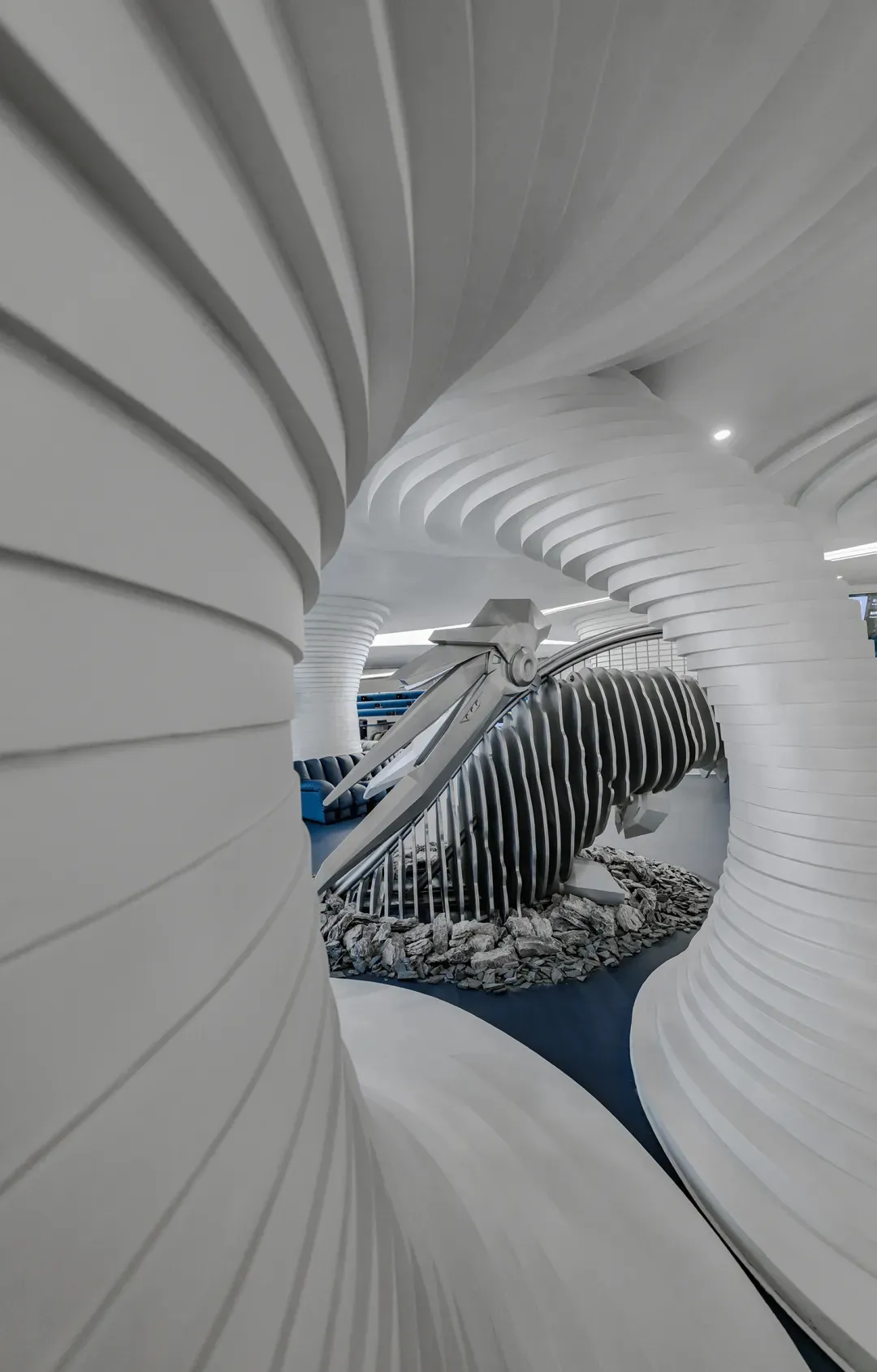 A white, spiral indoor space with a black, futuristic sculpture resembling a tornado in the center.