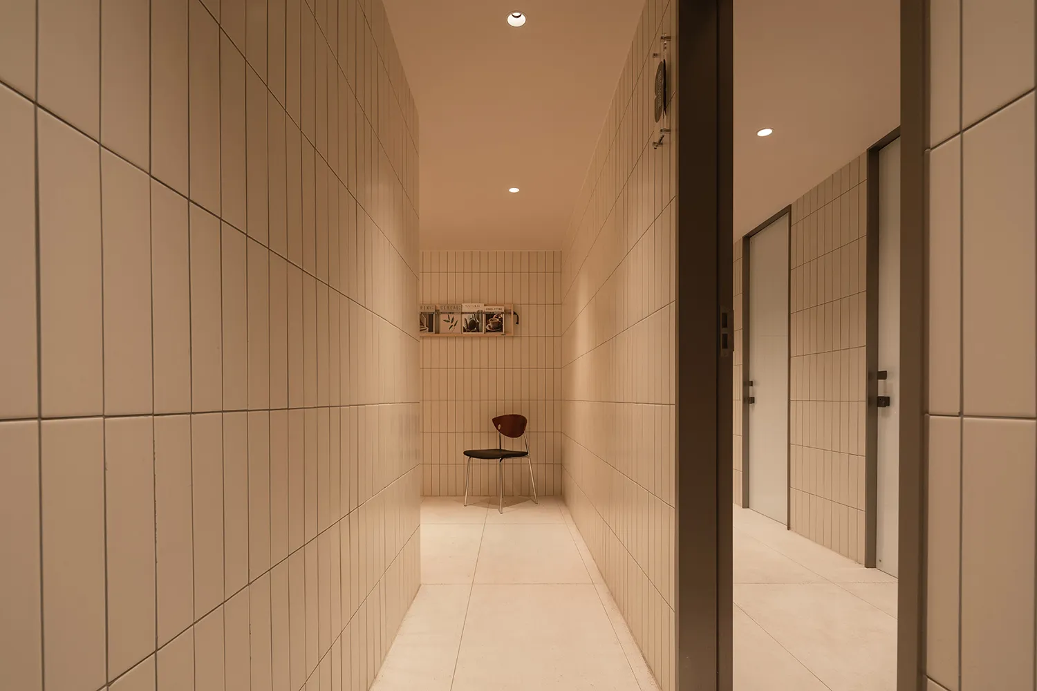 A minimalist corridor with tiled walls and a single chair in the distance.