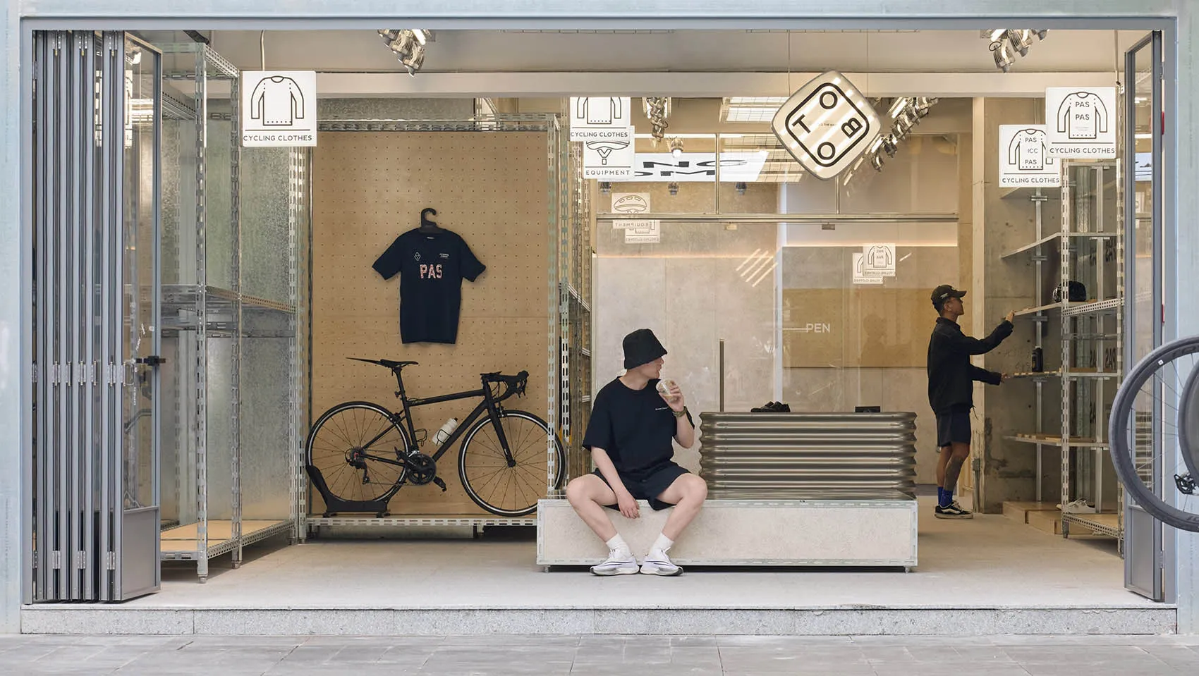 A modern retail storefront with glass walls showcasing a selection of clothing and a bicycle parked inside.