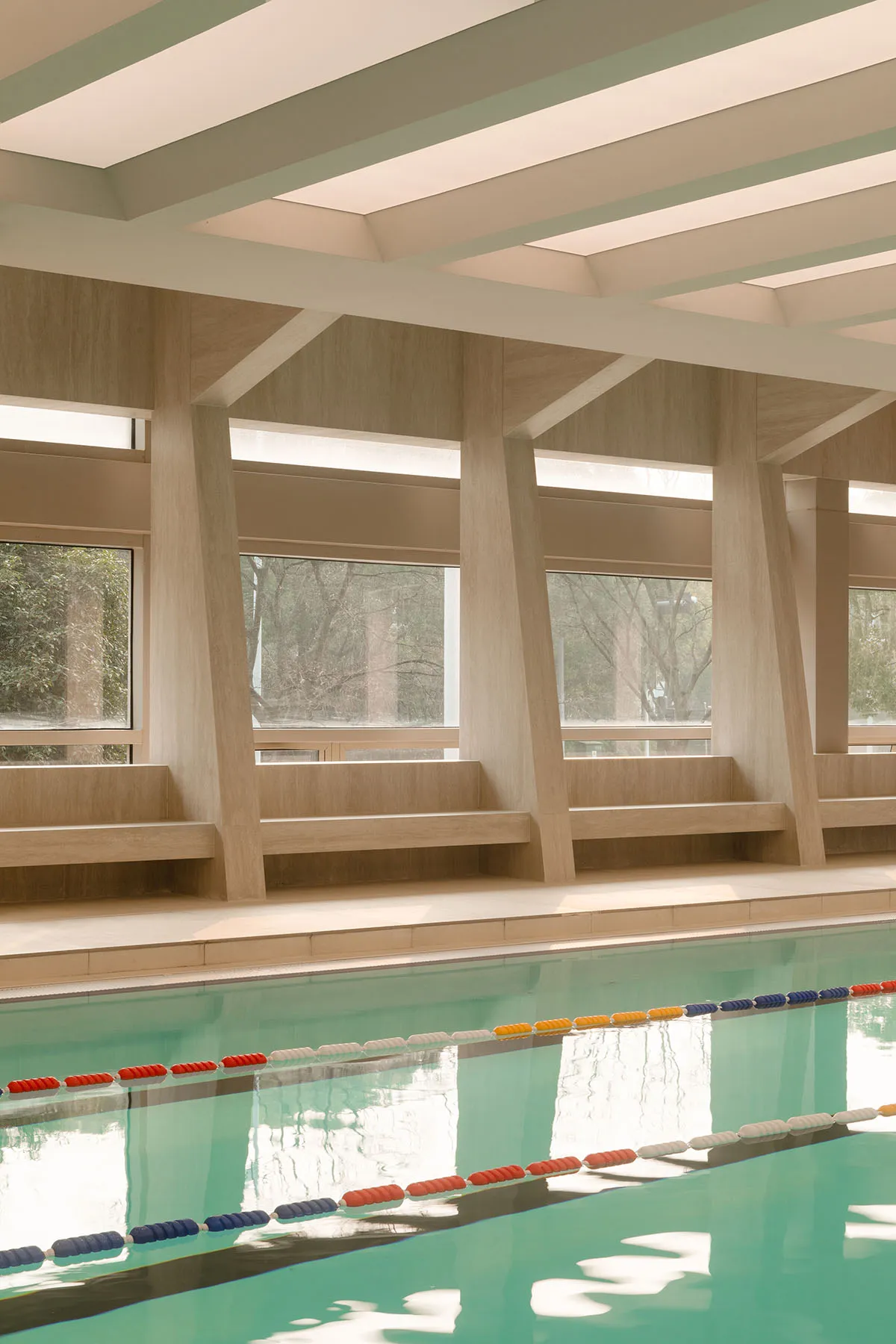 A modern indoor swimming pool with wooden beams and a view of the outdoors through large windows.