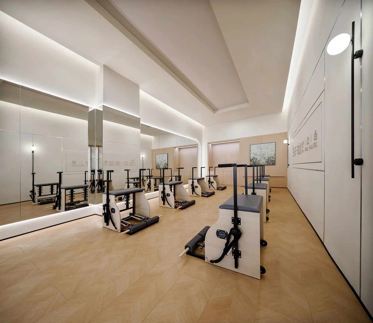 A minimalist fitness studio with hardwood floors features modern Pilates Reformers and mirrors.