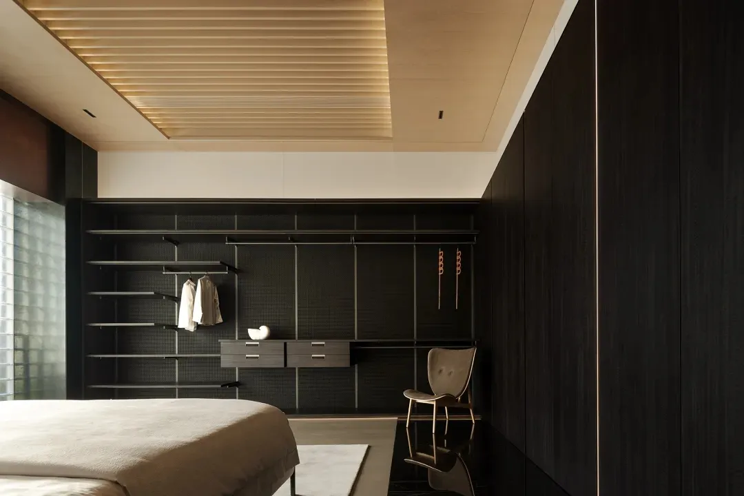 Minimalist bedroom with black wood walls and ceiling, light-colored bed and rug, and floating shelves with clothes.