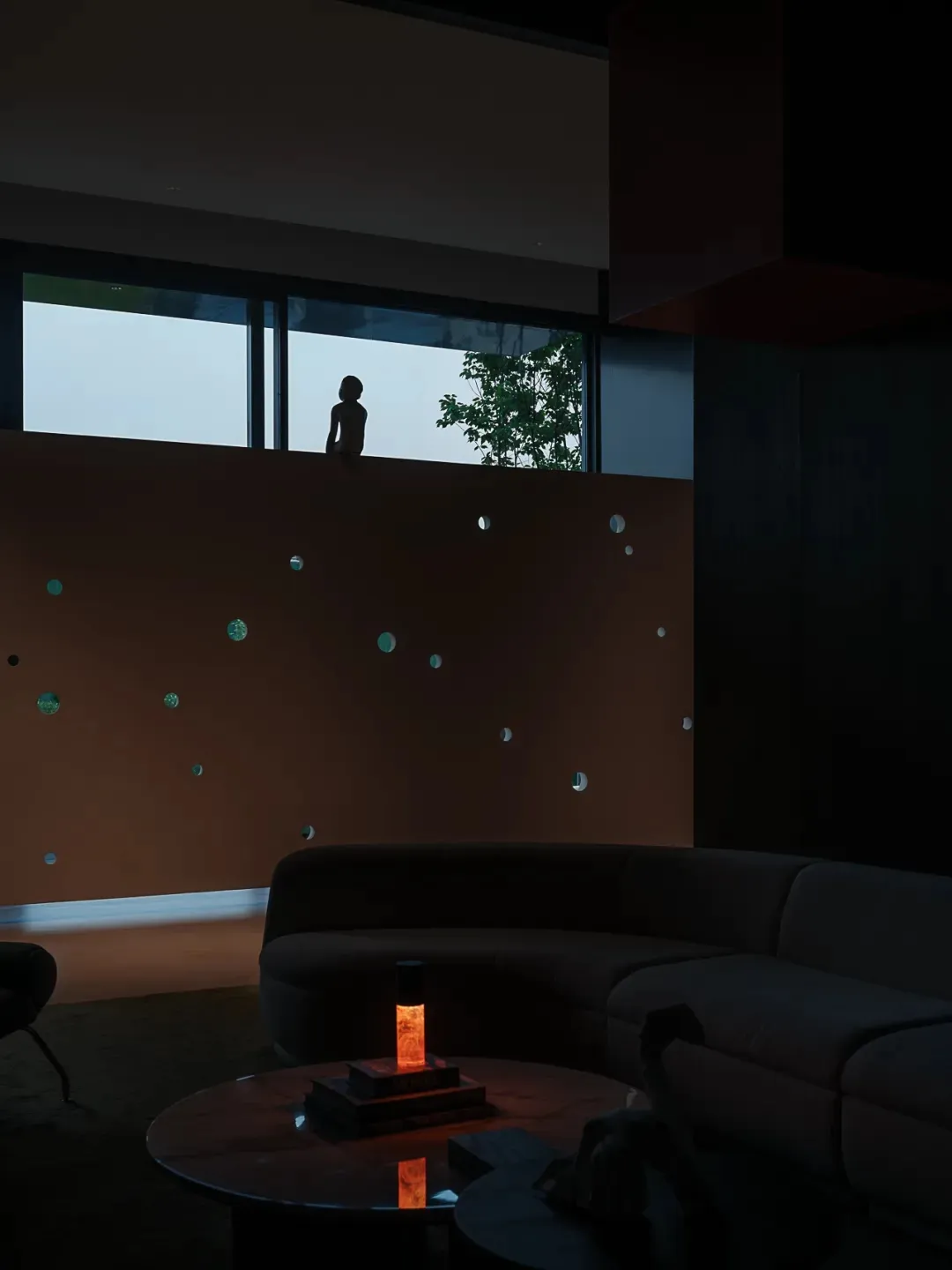 A minimalist modern living room featuring concrete walls and surfaces, with a large circular coffee table and a silhouette of