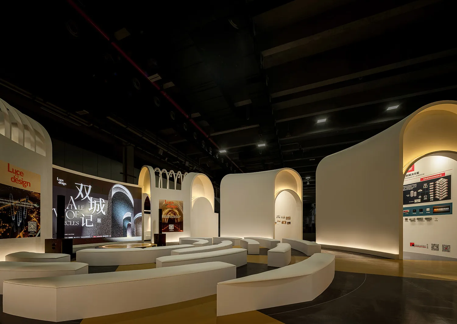 A minimalist exhibition space featuring white curved walls and soft seating.