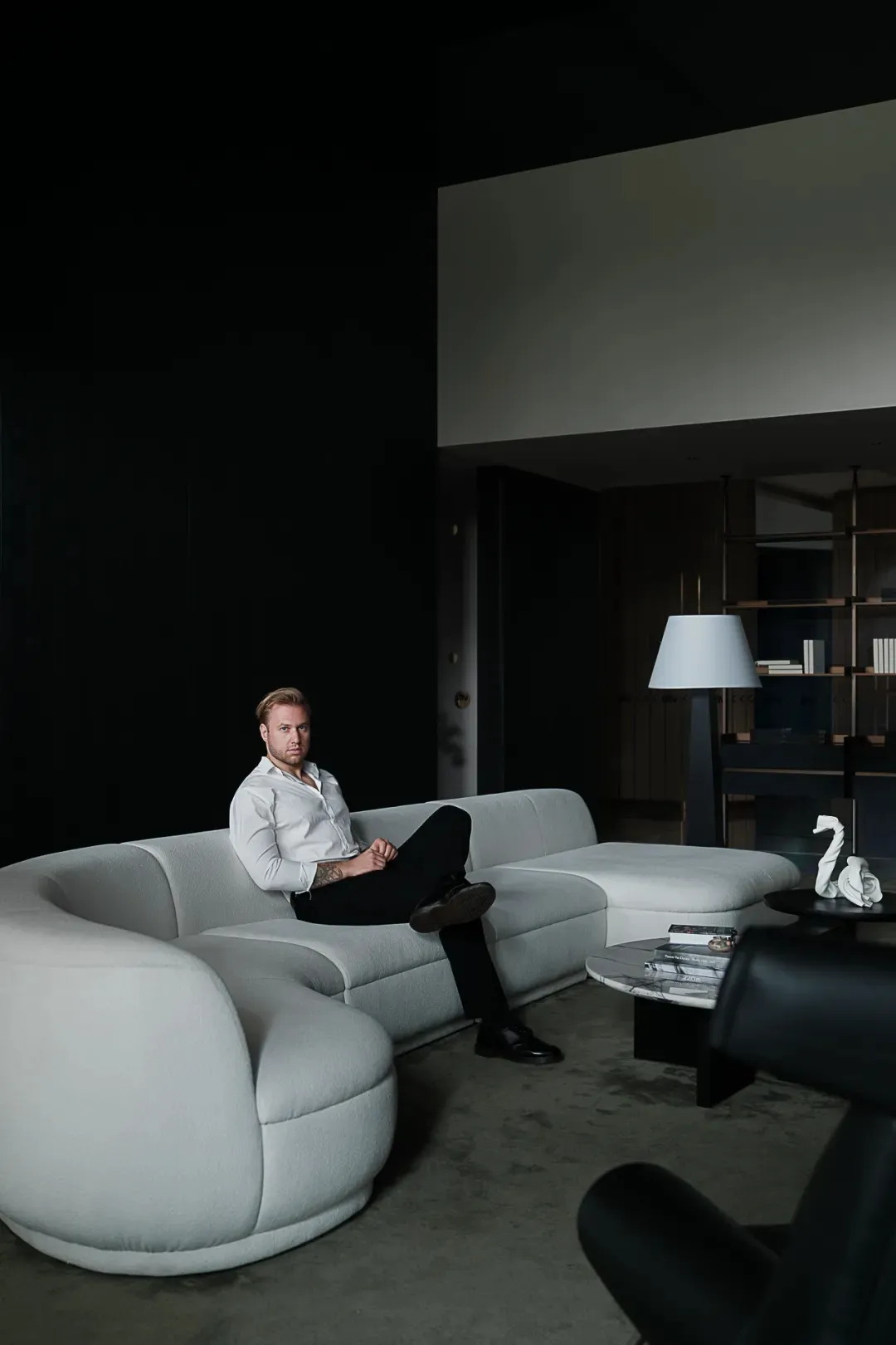 A minimalist living room featuring a white sofa, black coffee table, and dark, modern flooring.