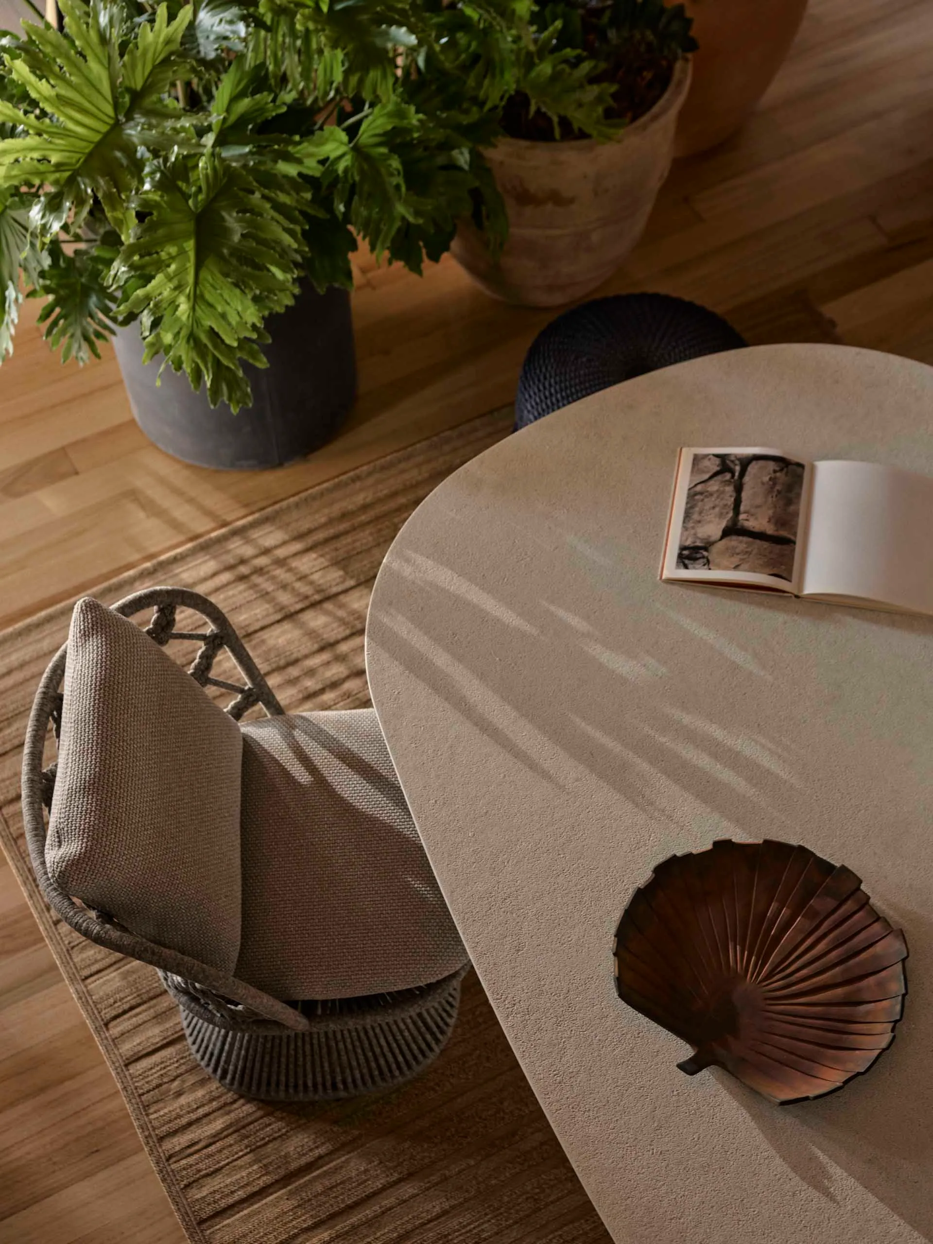 A modern setting featuring a sleek, circular concrete table with a small book and a decorative shell, surrounded by woven arm