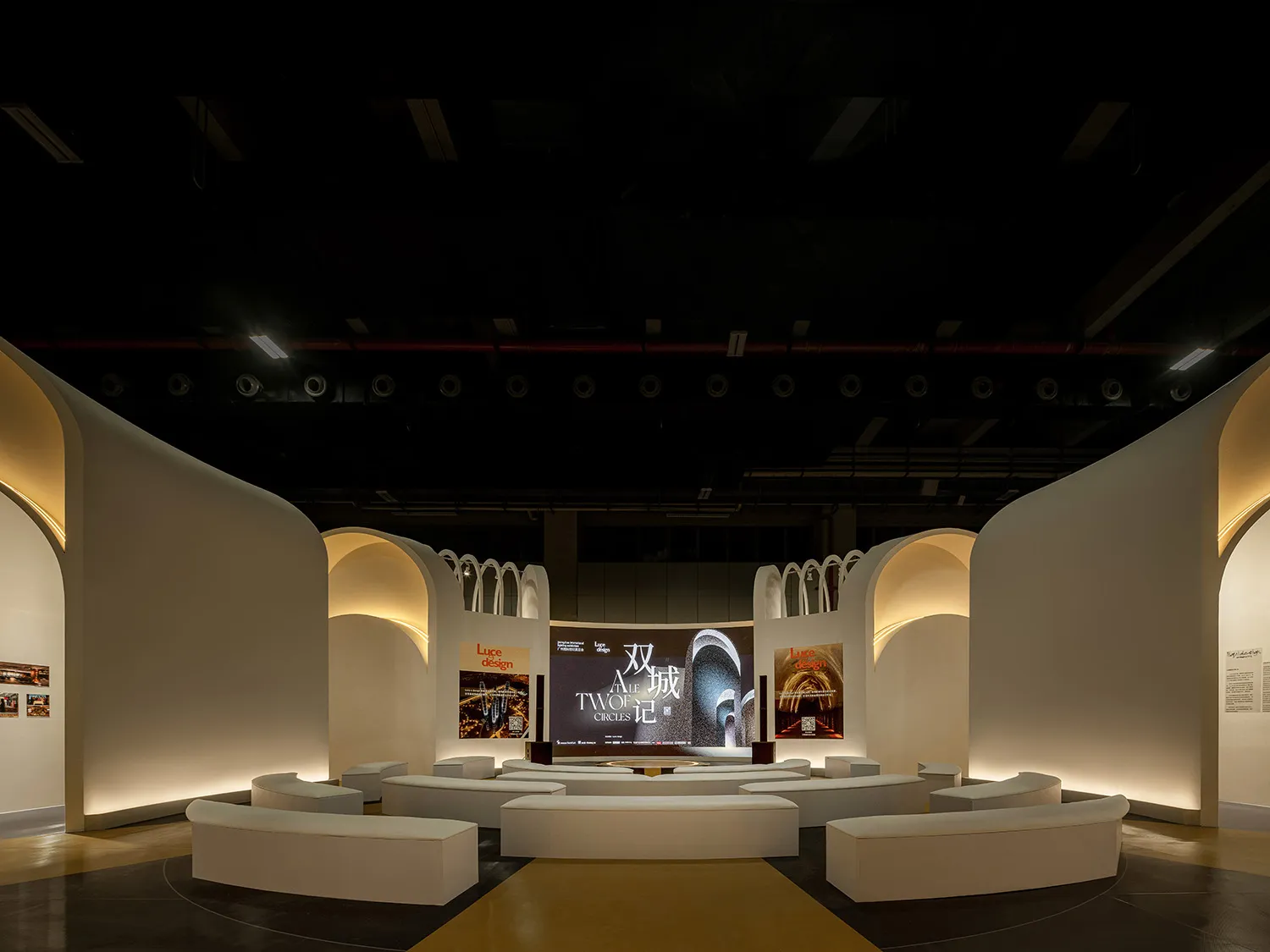 A modern exhibition space with circular seating, a central stage, and illuminated archways.
