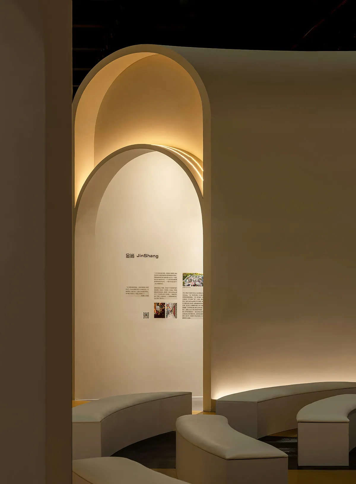 A modern exhibition space with light-colored stone walls and curved seating.