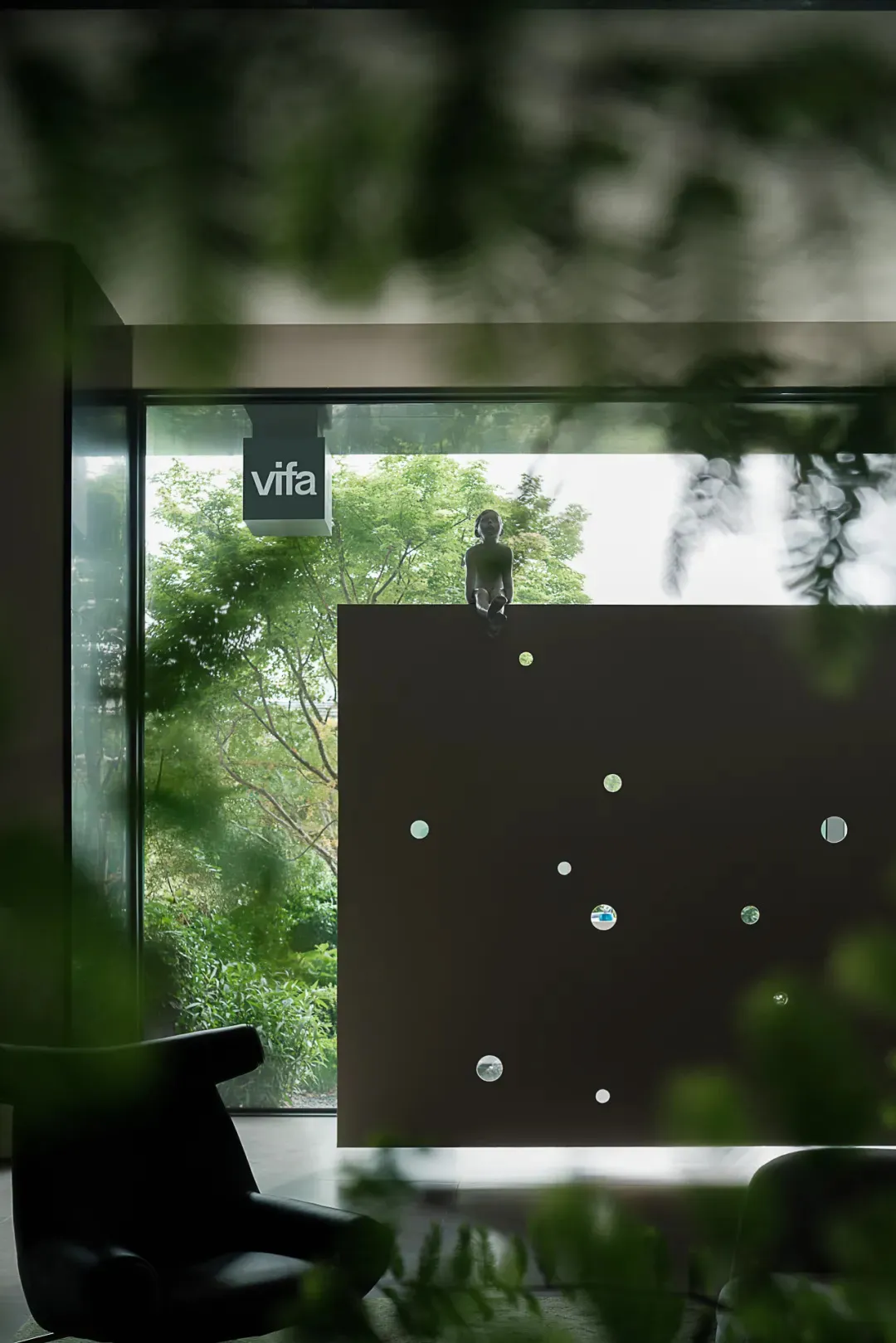 A modern interior design featuring a glass wall overlooking greenery and a minimalist black partition with circular cutouts.