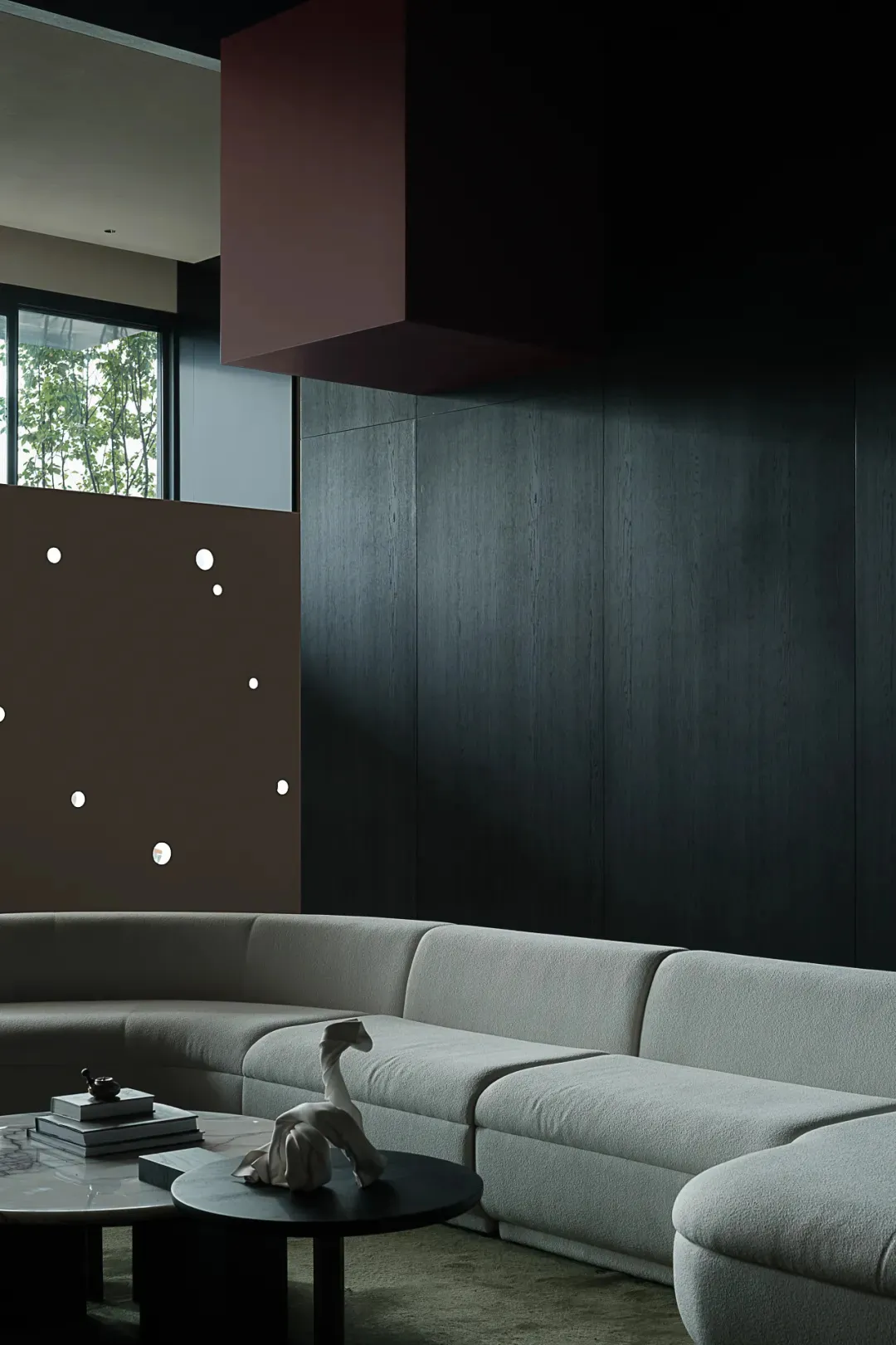 Modern living room featuring a cushioned sofa against a dark, minimalist background with a large window.