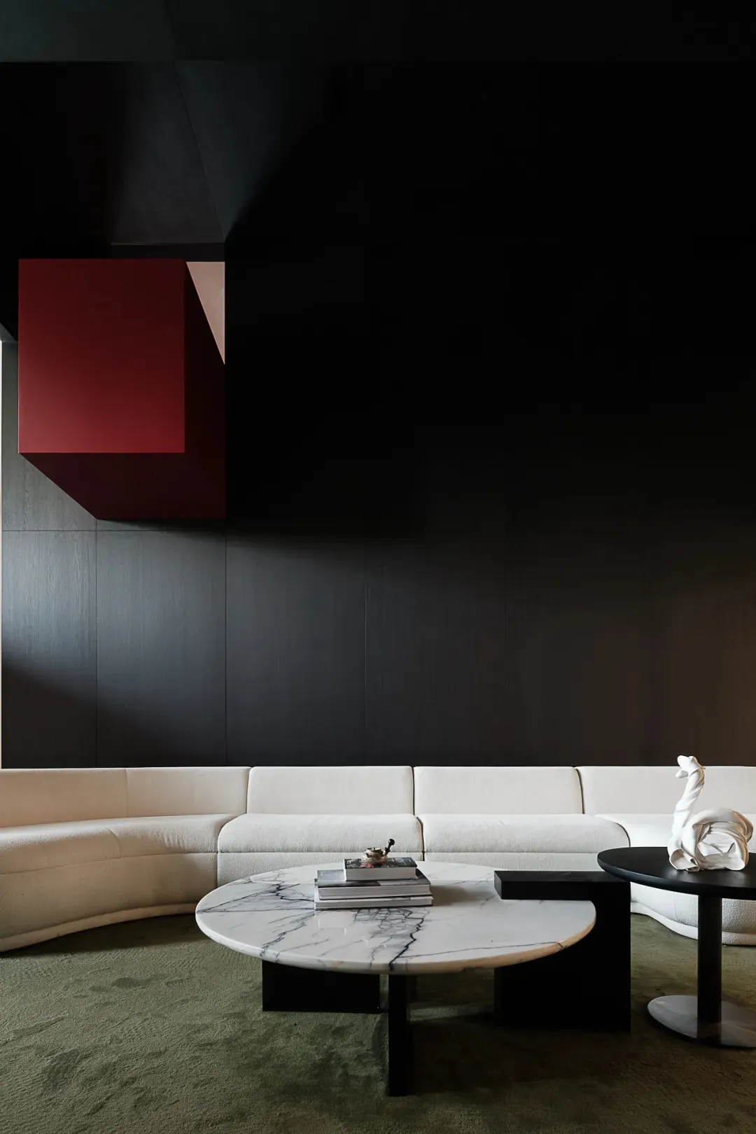 Modern living room with white and red modular seating, a round marble coffee table, and dark green carpet.