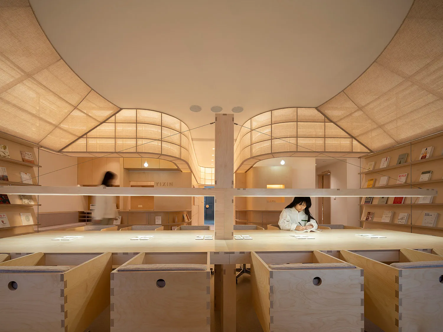 A modern library interior with wooden elements and light-colored fabric ceilings.