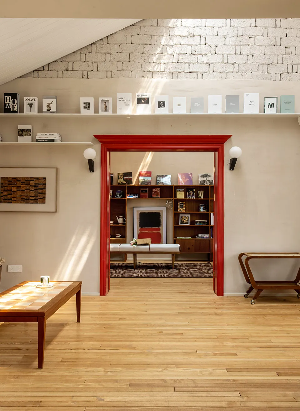 A modern living room with wooden floors and furniture, showcasing a white bench, a coffee table, and a bookshelf filled with