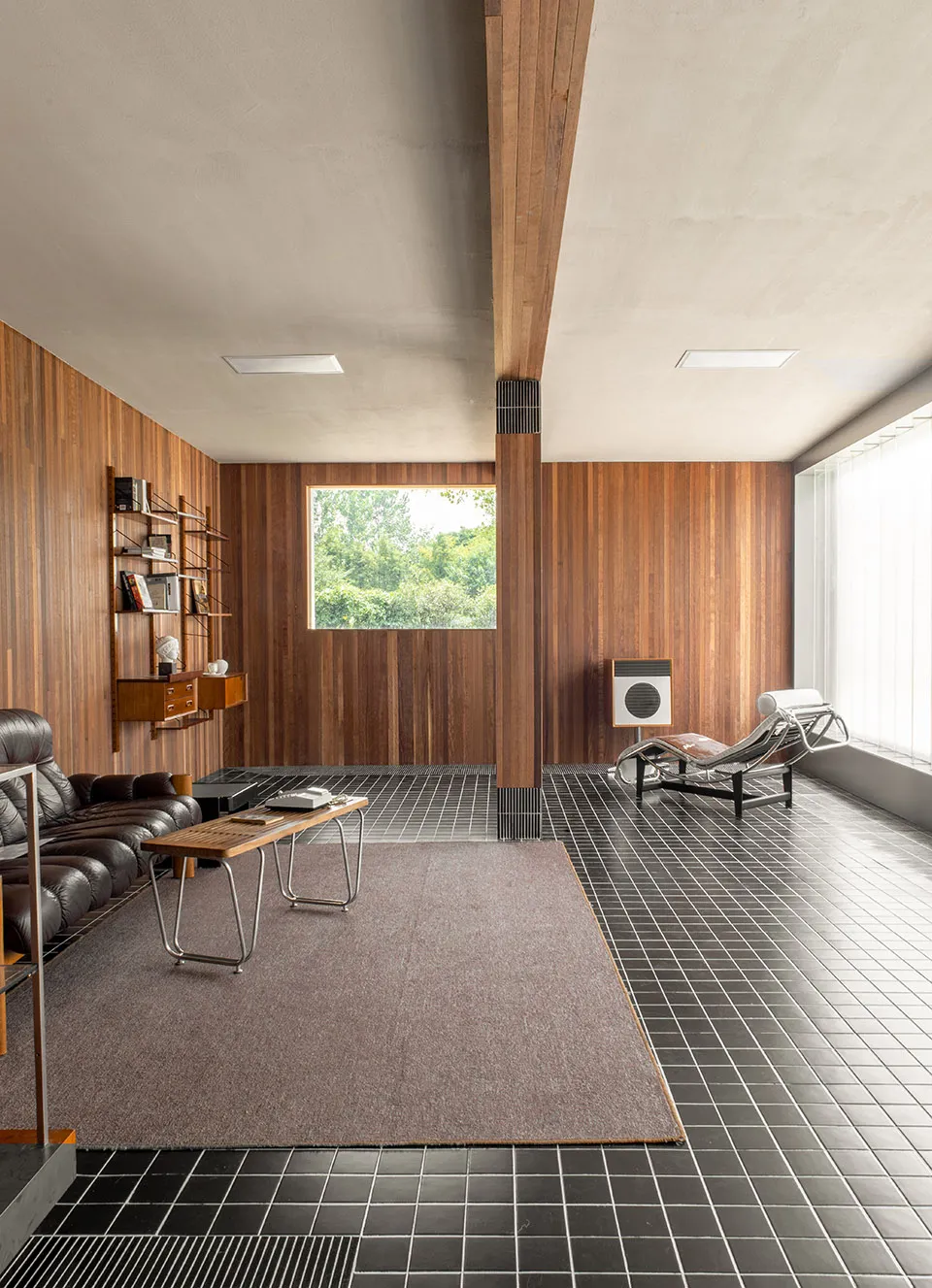 A modern living room with wooden walls and tiled flooring, featuring a black leather sofa, a wooden coffee table, a wall-moun