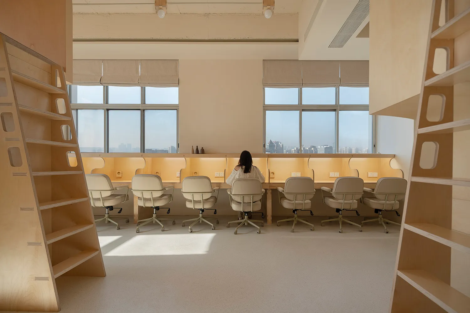 A spacious, industrial-style workspace featuring wooden furniture and a long desk with a view of the city.