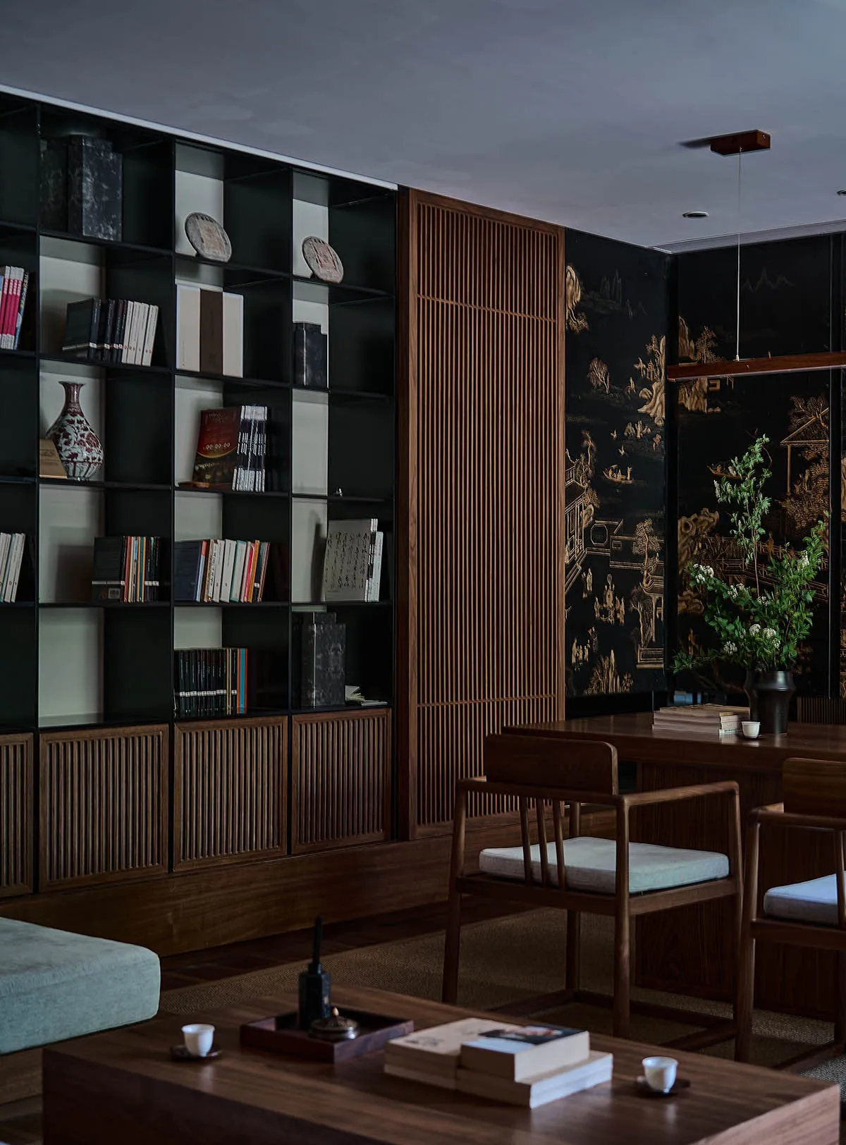 A modern living room featuring a black bookshelf with various books and decorative items, accompanied by wooden furniture and