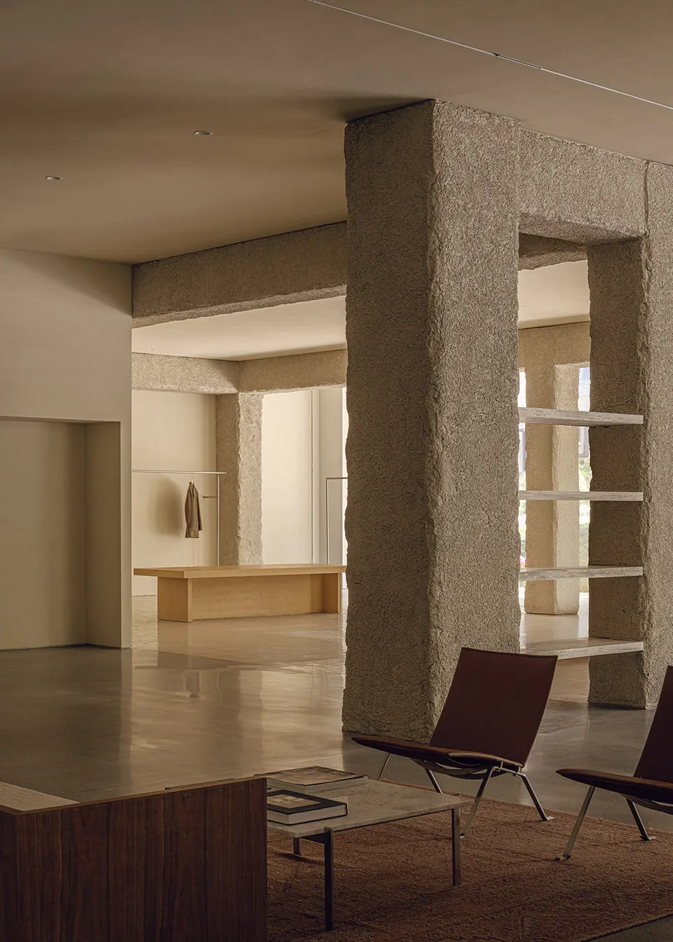 A modern office space featuring minimalist furniture and concrete columns with natural light streaming through the windows.