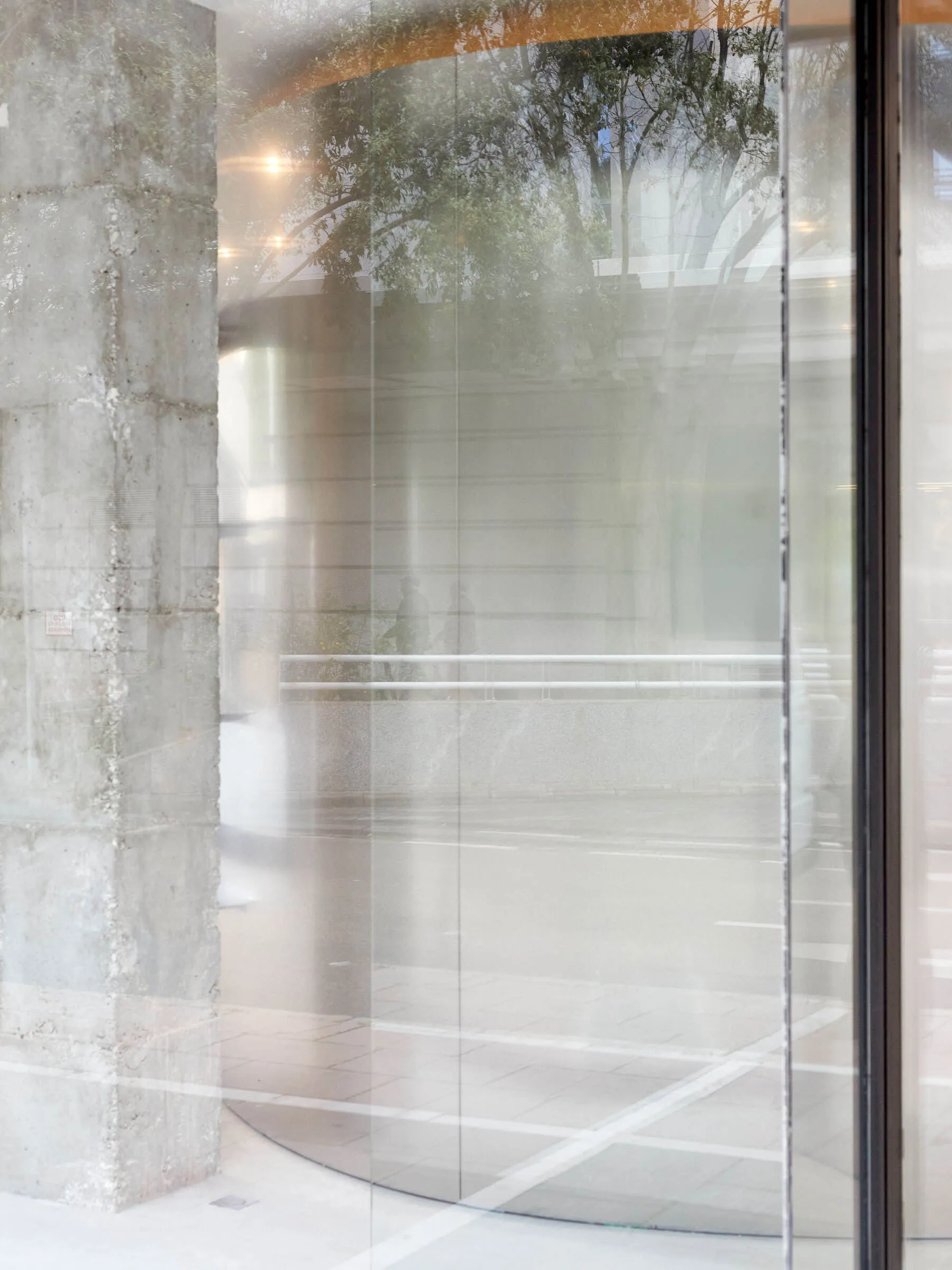 A view of a street captured through a mirrored glass window, reflecting trees and a building.