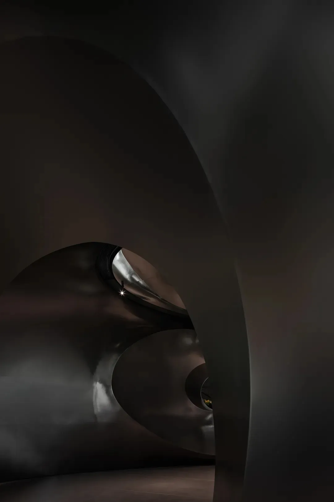 A curved, metallic architectural interior with dark, smooth surfaces