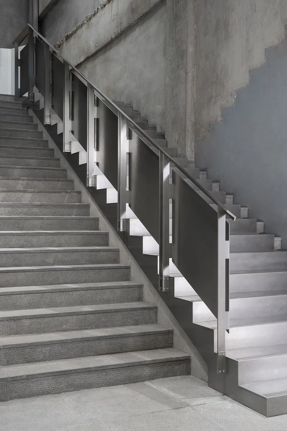 Staircase with industrial design, featuring metal railings and concrete steps on a concrete floor.
