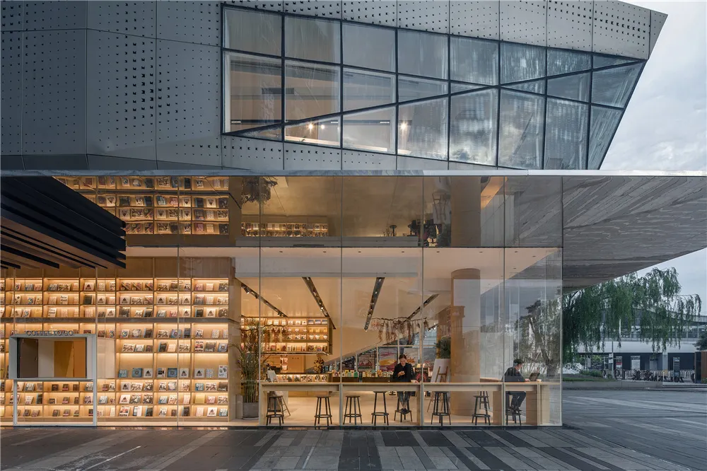 A modern coffee shop with large glass windows and a wooden interior, featuring a bar area with stools and a small table.