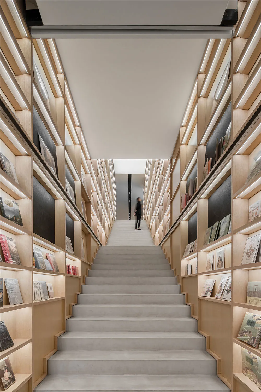 Modern library with stairs and wooden shelves filled with books.